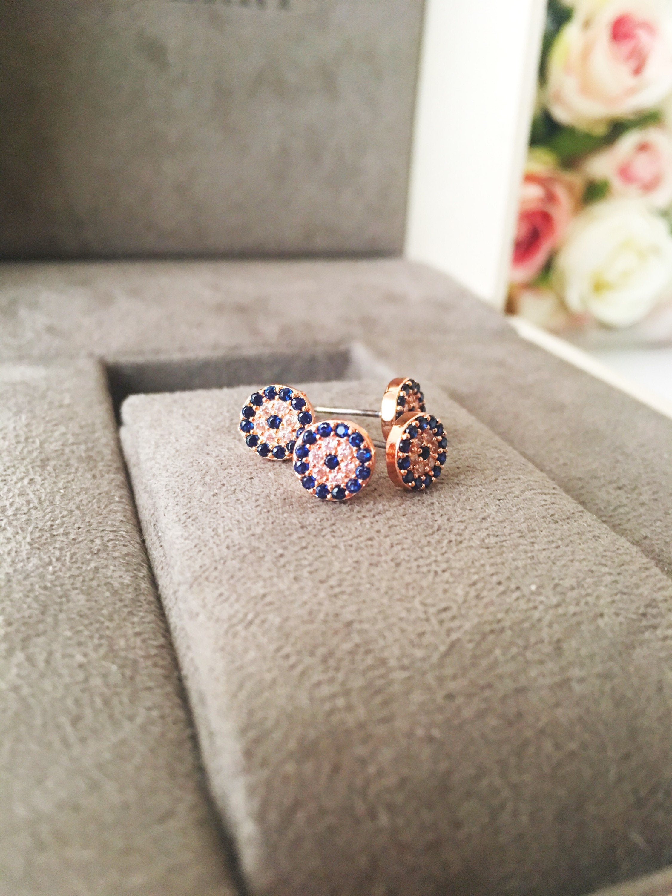 A pair of handmade evil eye stud earrings in silver and rose gold, featuring a tiny 7mm design with zircon embellishments, symbolizing protection.