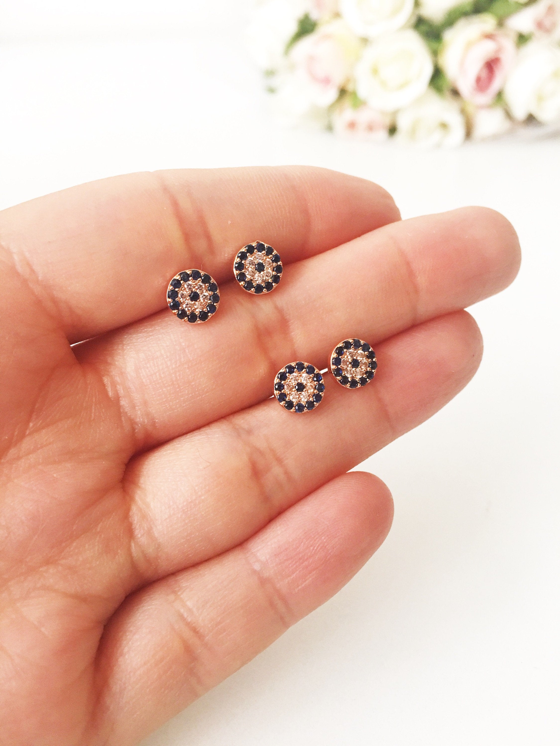 A pair of handmade evil eye stud earrings in silver and rose gold, featuring a tiny 7mm design with zircon embellishments, symbolizing protection.