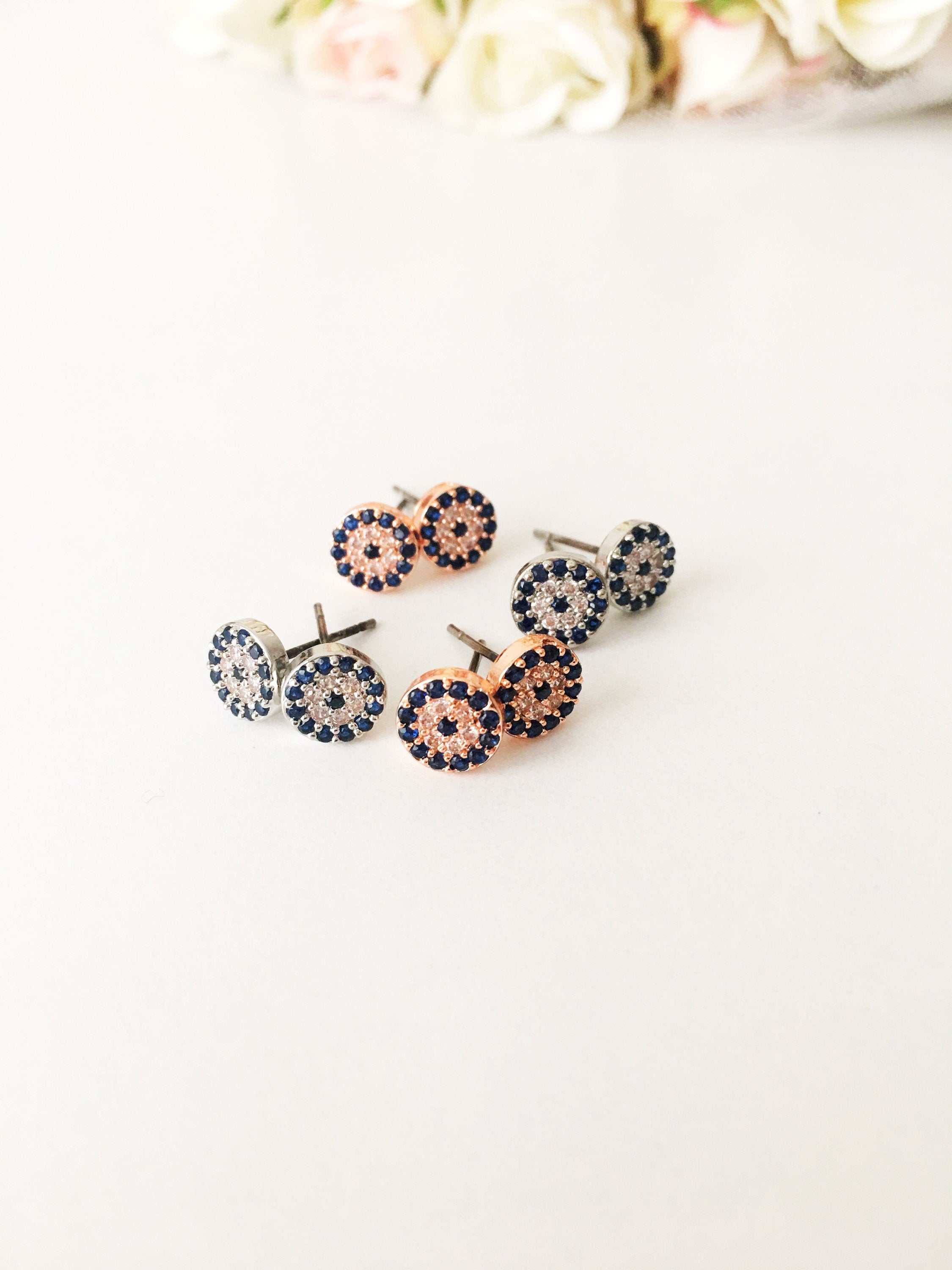 A pair of handmade evil eye stud earrings in silver and rose gold, featuring a tiny 7mm design with zircon embellishments, symbolizing protection.