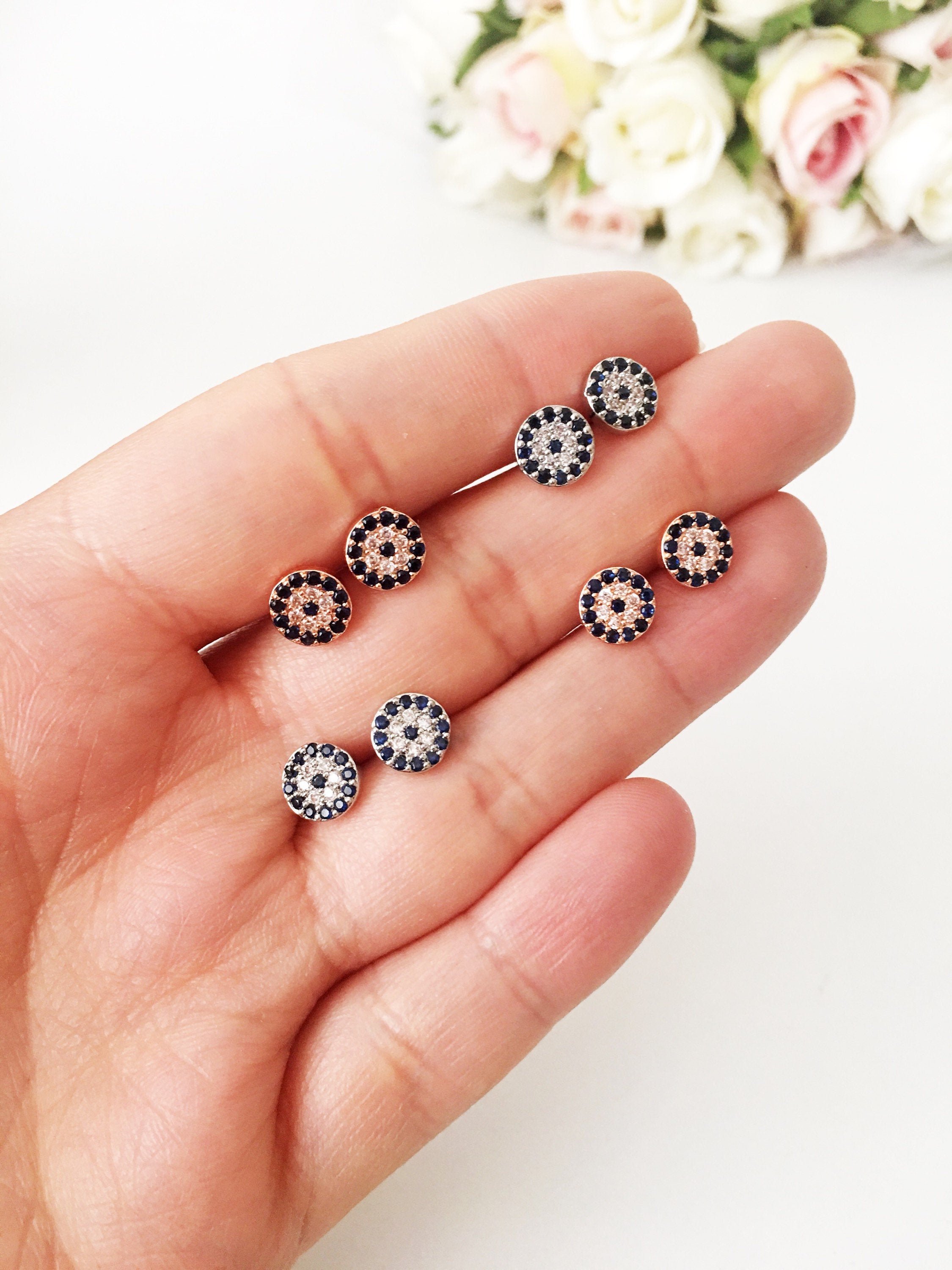 A pair of handmade evil eye stud earrings in silver and rose gold, featuring a tiny 7mm design with zircon embellishments, symbolizing protection.