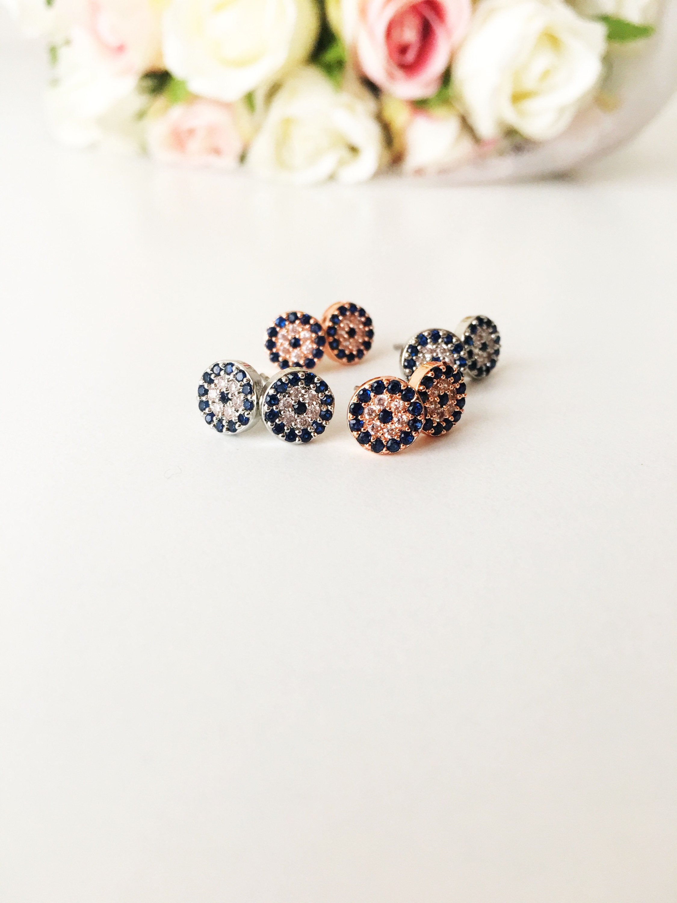 A pair of handmade evil eye stud earrings in silver and rose gold, featuring a tiny 7mm design with zircon embellishments, symbolizing protection.