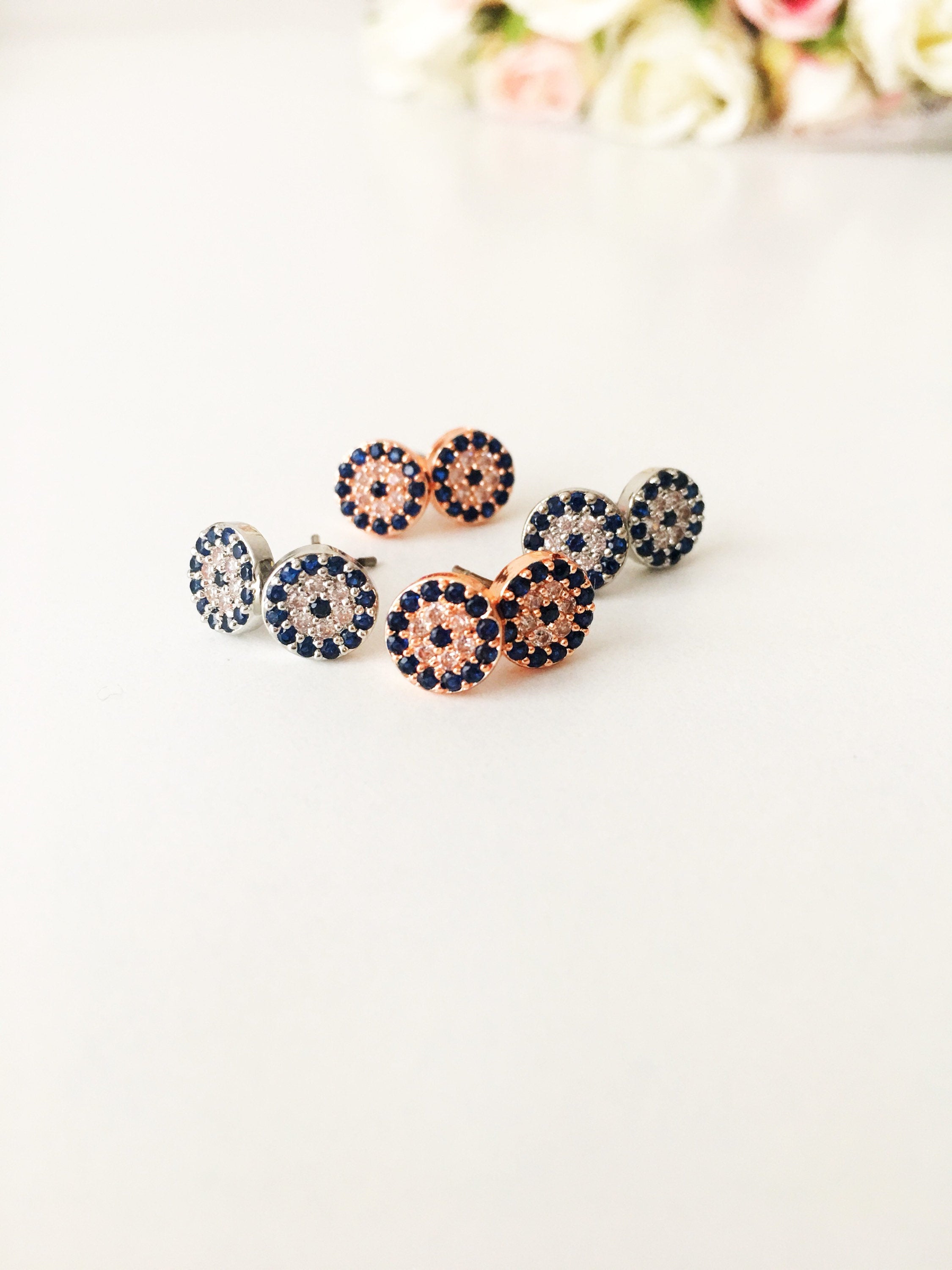 A pair of handmade evil eye stud earrings in silver and rose gold, featuring a tiny 7mm design with zircon embellishments, symbolizing protection.