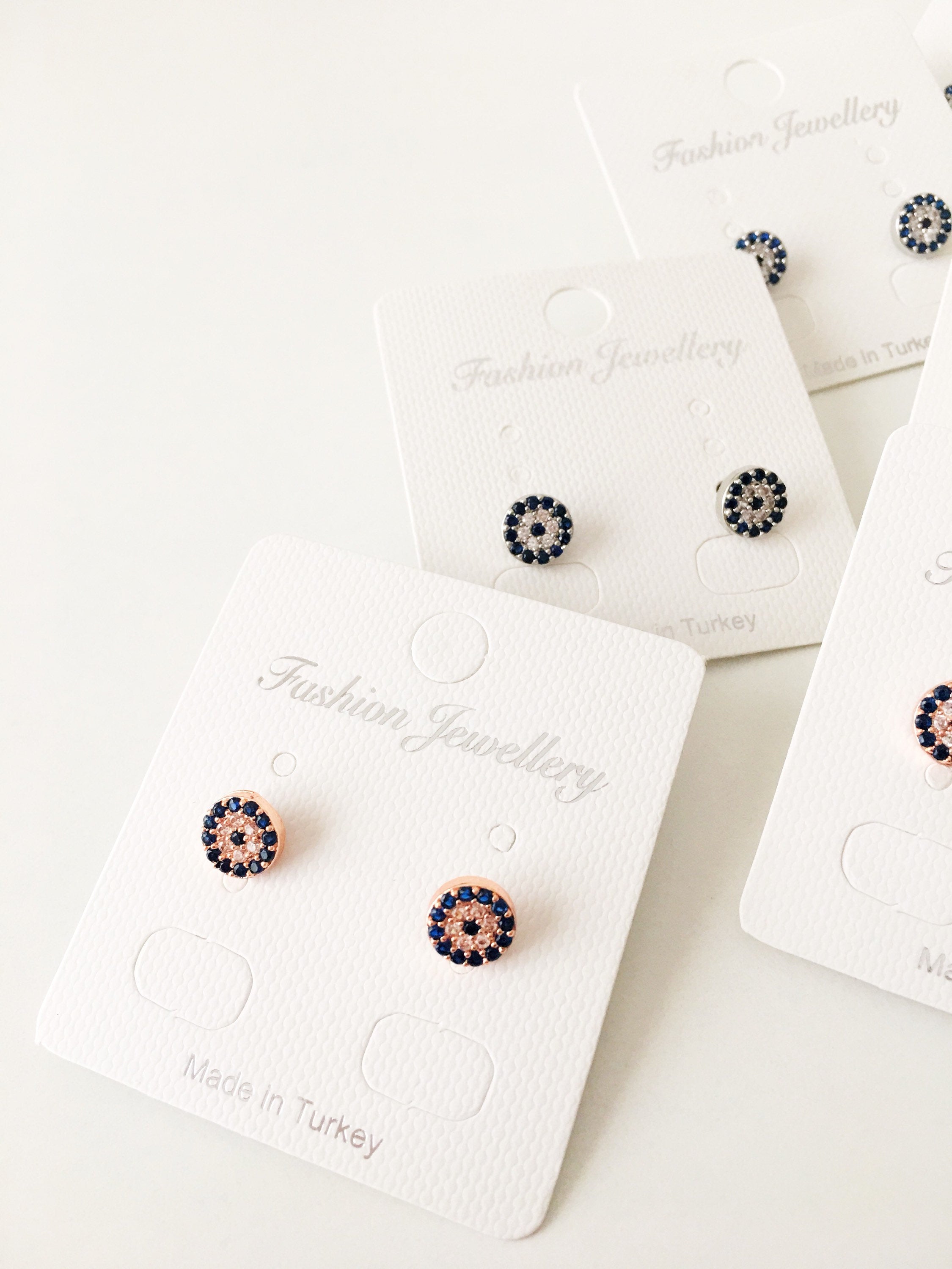 A pair of handmade evil eye stud earrings in silver and rose gold, featuring a tiny 7mm design with zircon embellishments, symbolizing protection.