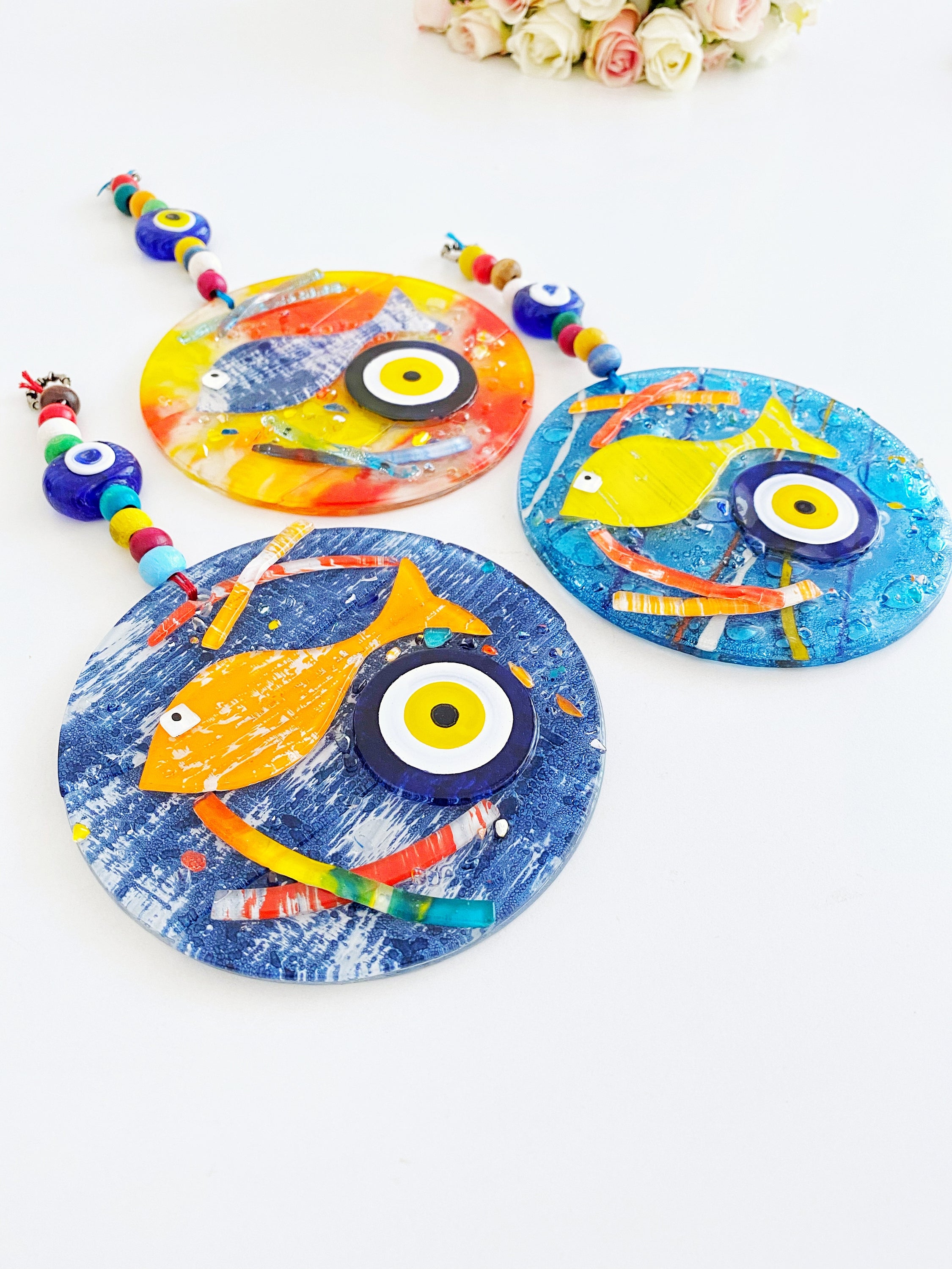 Handmade fused glass Evil Eye wall hanging featuring a fish design, vibrant colors, and unique craftsmanship, measuring 12cm x 12cm.