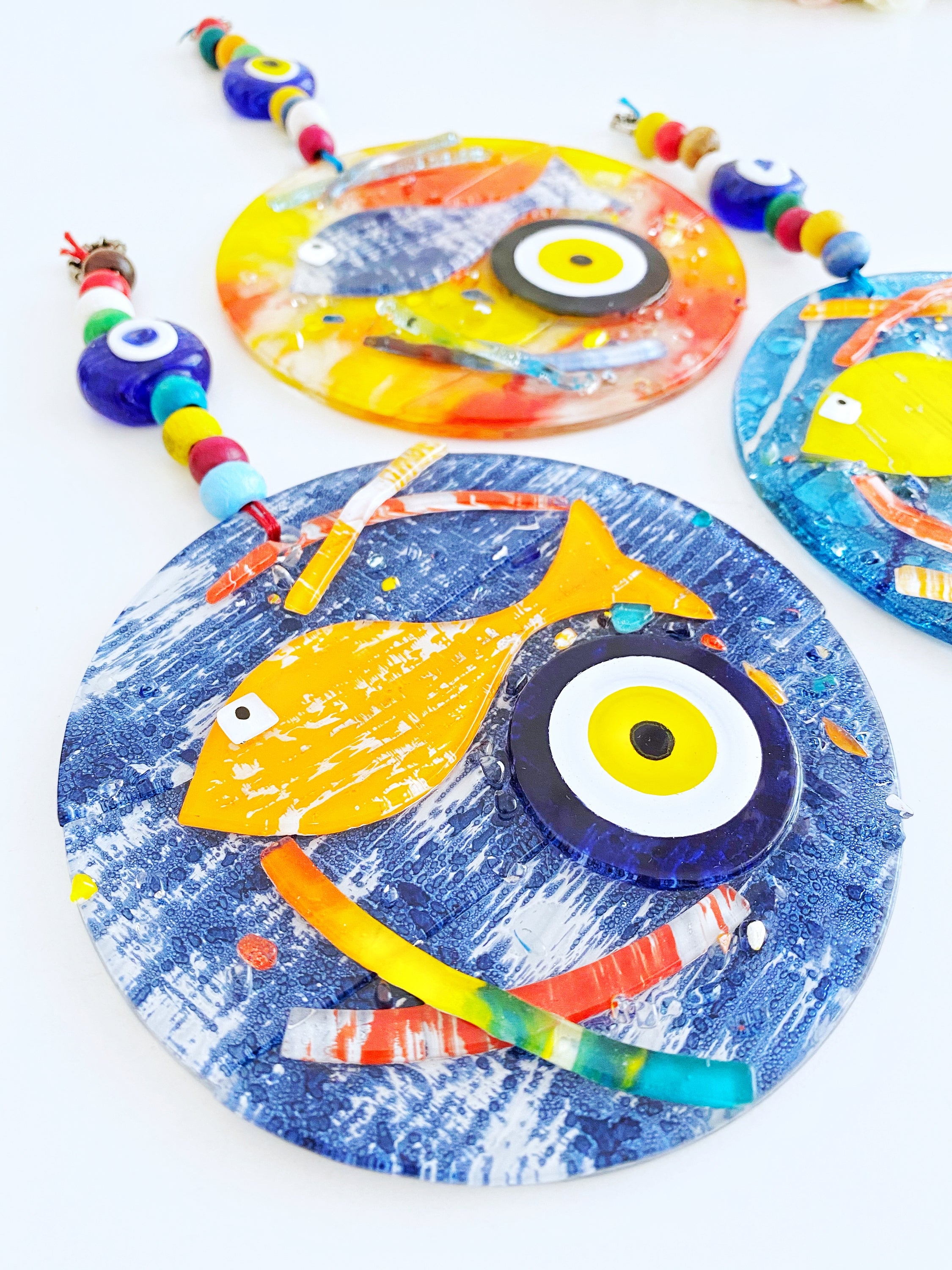 Handmade fused glass Evil Eye wall hanging featuring a fish design, vibrant colors, and unique craftsmanship, measuring 12cm x 12cm.