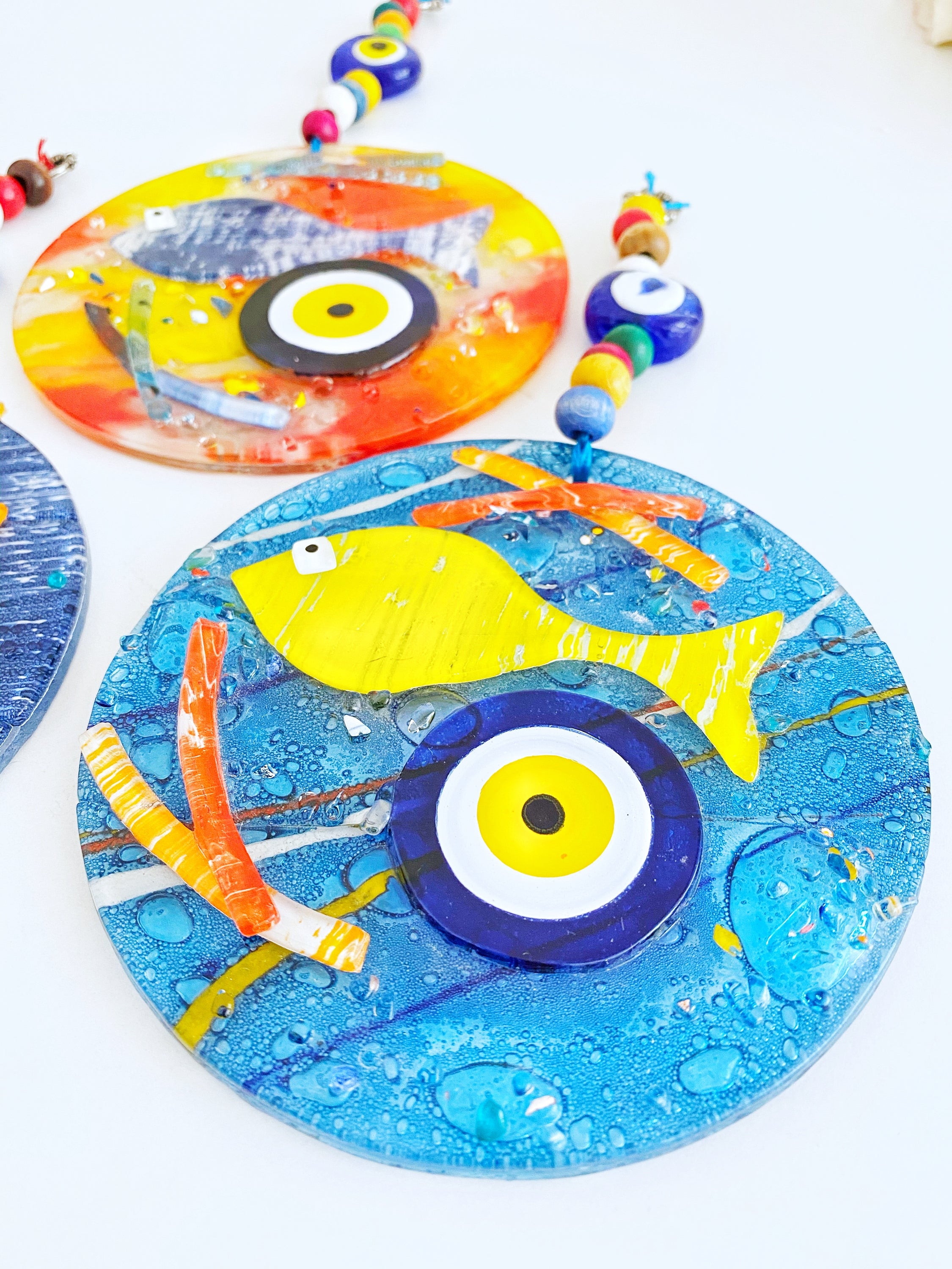 Handmade fused glass Evil Eye wall hanging featuring a fish design, vibrant colors, and unique craftsmanship, measuring 12cm x 12cm.