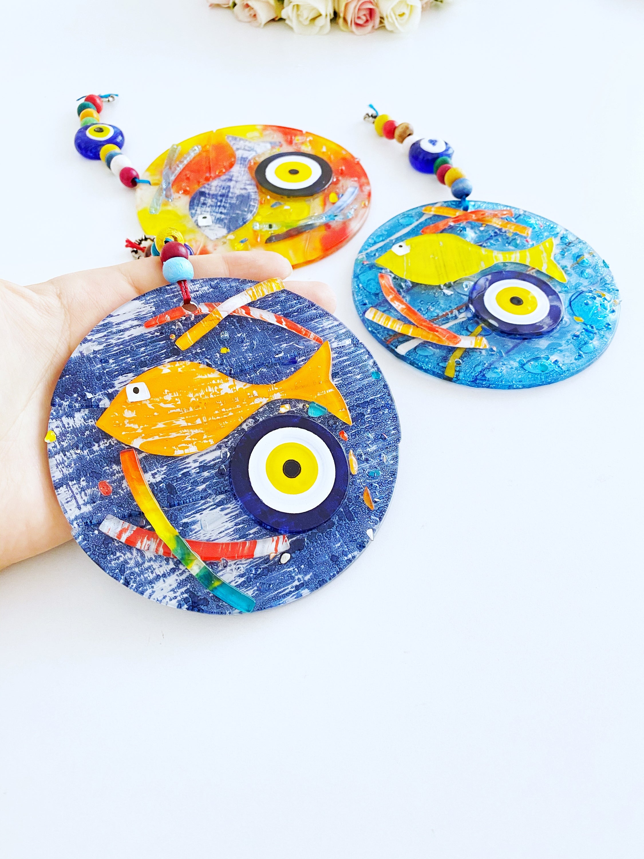 Handmade fused glass Evil Eye wall hanging featuring a fish design, vibrant colors, and unique craftsmanship, measuring 12cm x 12cm.