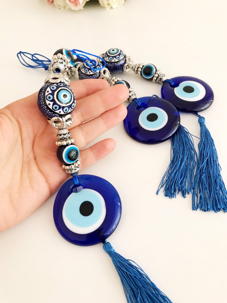 Handmade evil eye wall hanging featuring a blue ceramic evil eye bead and a ceramic ball, measuring 33cm in length.