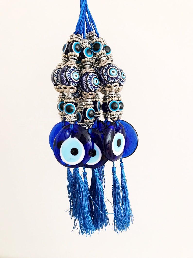 Handmade evil eye wall hanging featuring a blue ceramic evil eye bead and a ceramic ball, measuring 33cm in length.