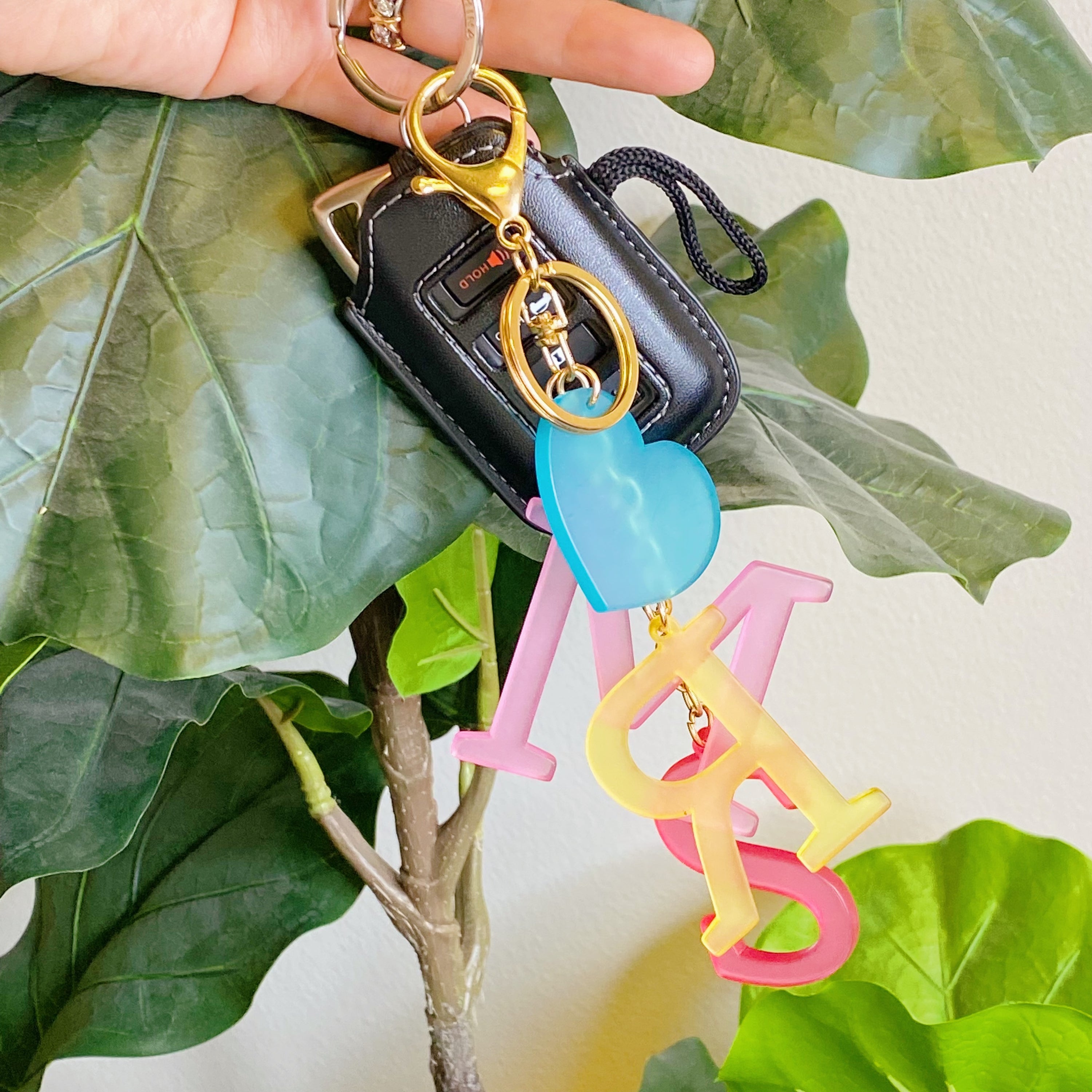 A stylish Favorite Word Jingle Key Chain featuring beautifully cut-out letters and gold tone hardware, perfect for keys or as a bag charm.