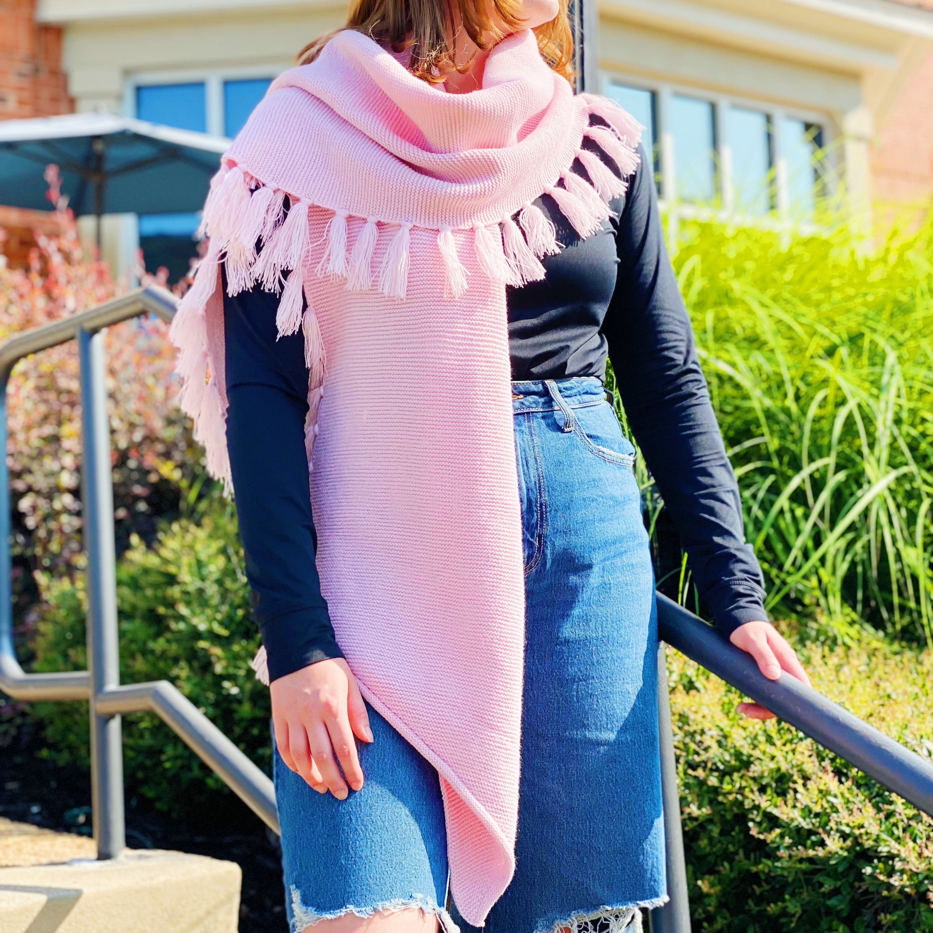 A cozy pink blanket scarf with fringes, showcasing its soft texture and stylish design, perfect for layering.