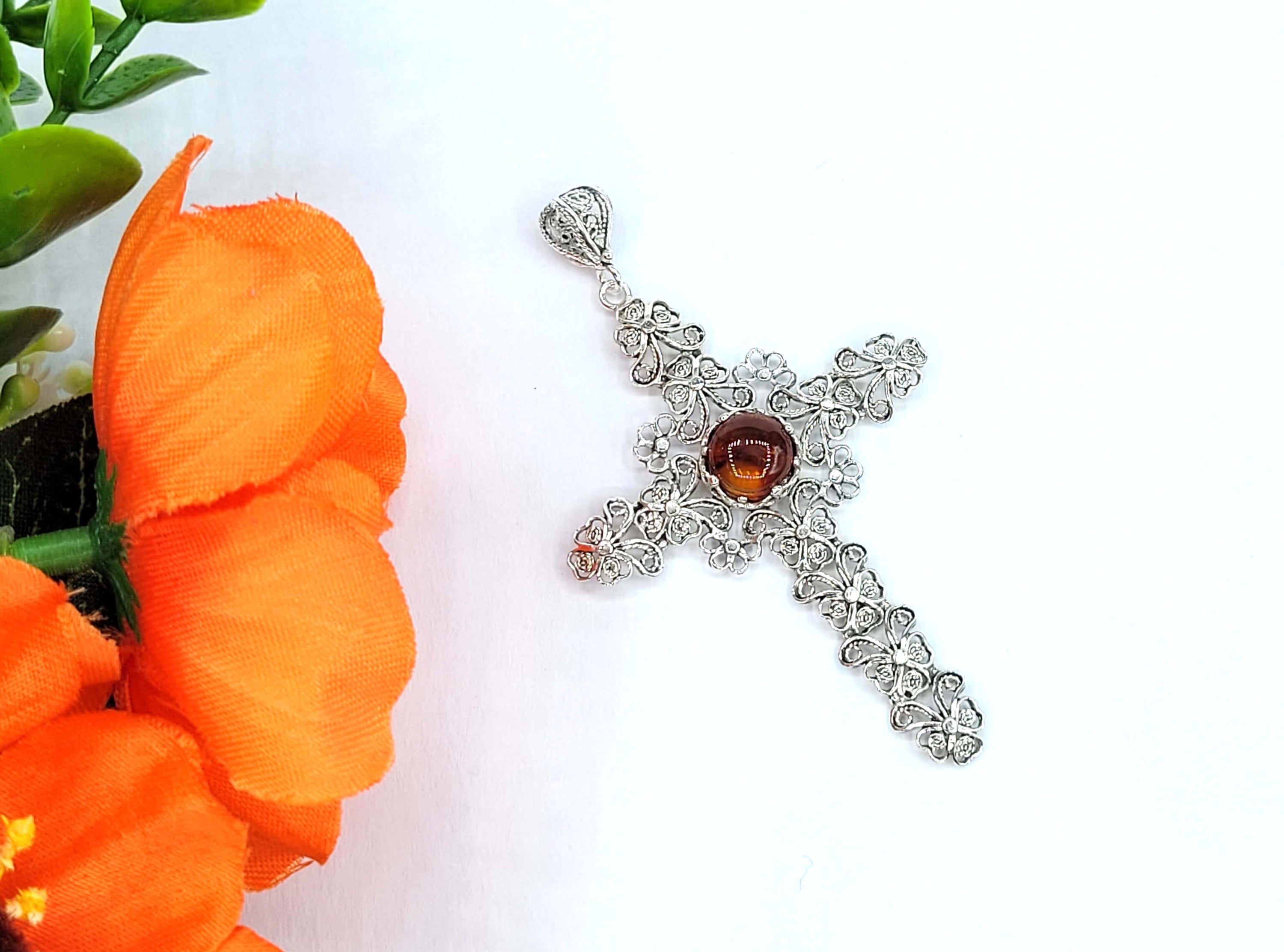 Elegant silver cross pendant necklace featuring intricate filigree design and a round amber stone centerpiece.