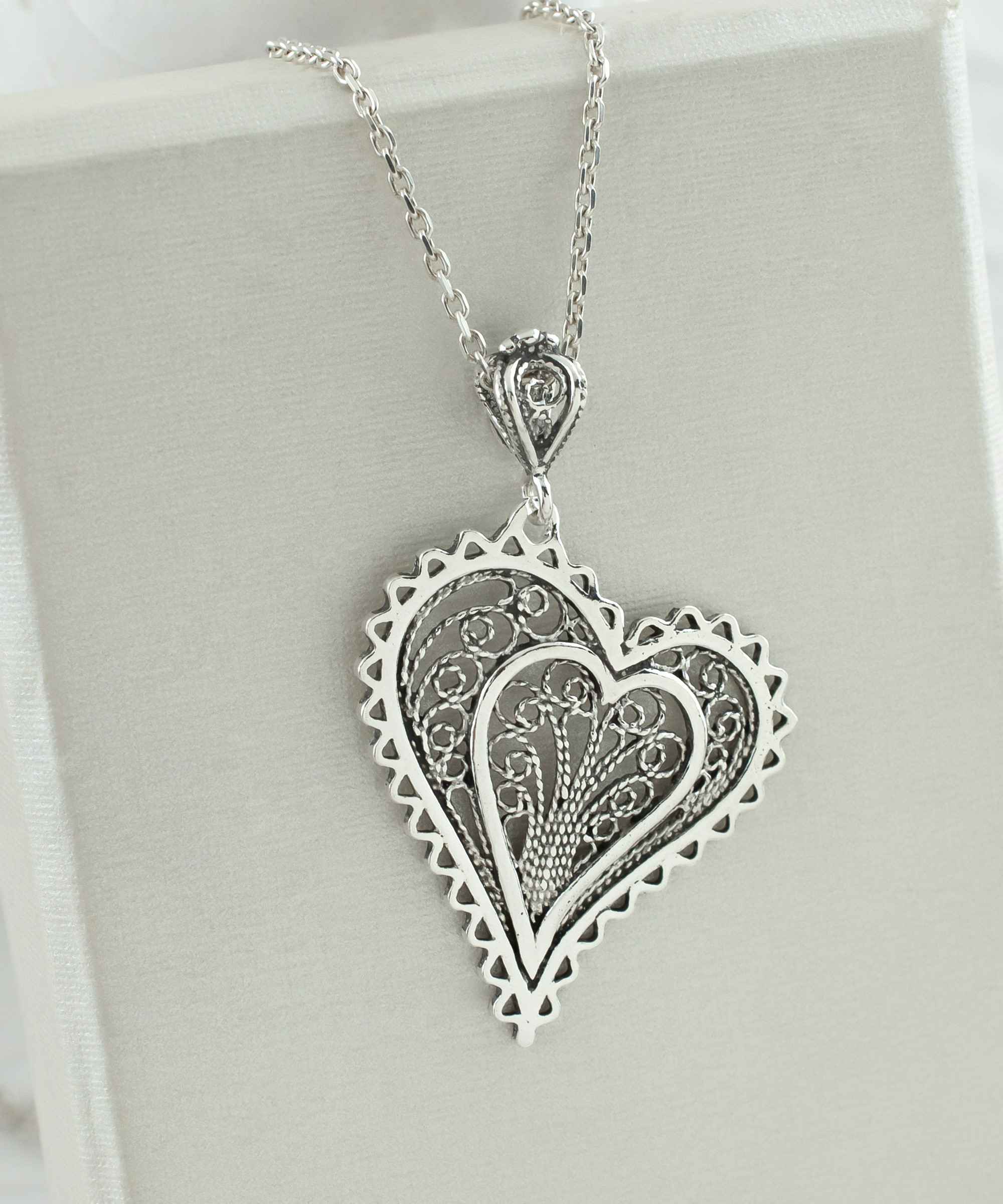 Elegant 925 Sterling Silver filigree heart pendant necklace with asymmetric design, displayed on a soft velvet background.