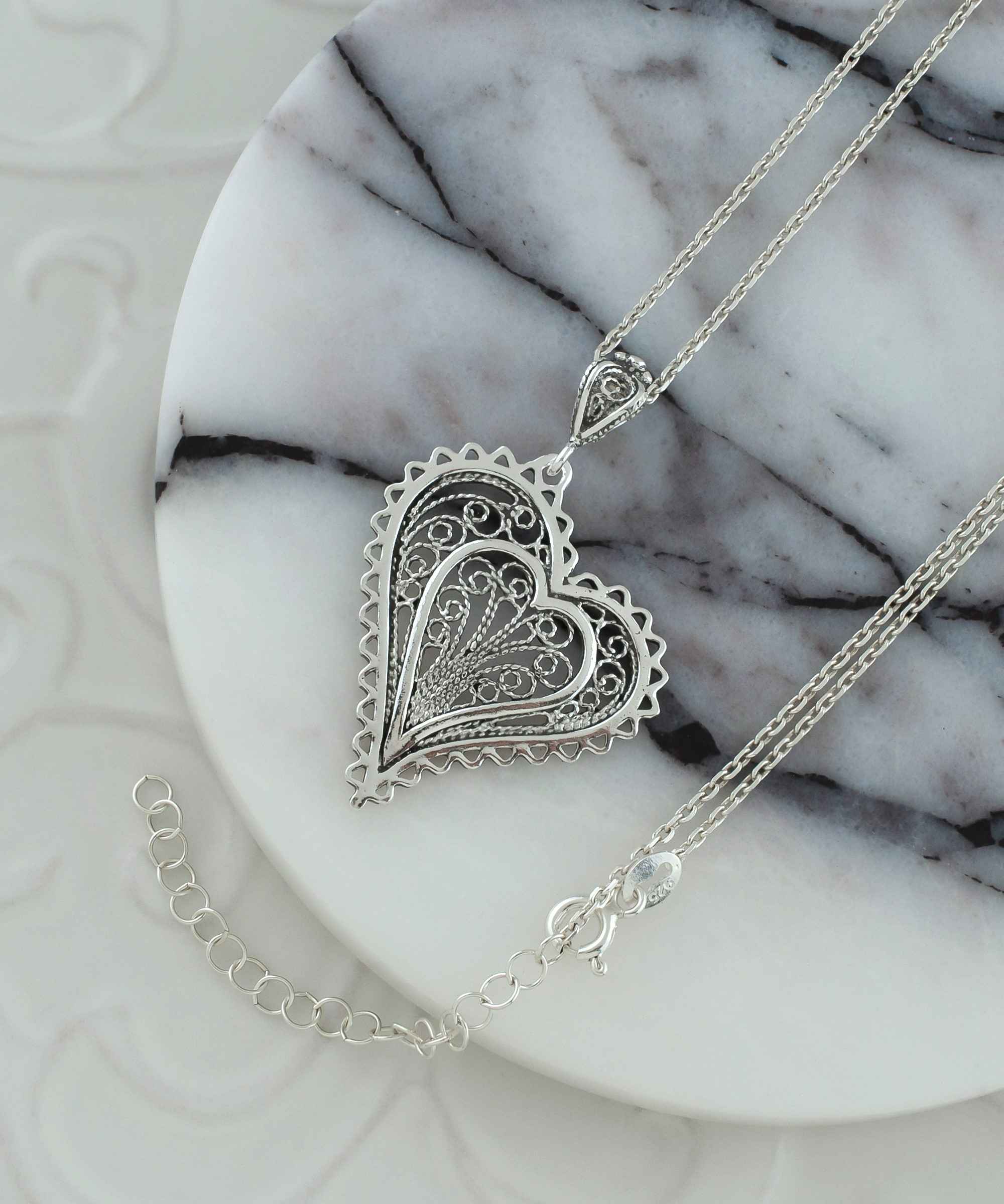 Elegant 925 Sterling Silver filigree heart pendant necklace with asymmetric design, displayed on a soft velvet background.