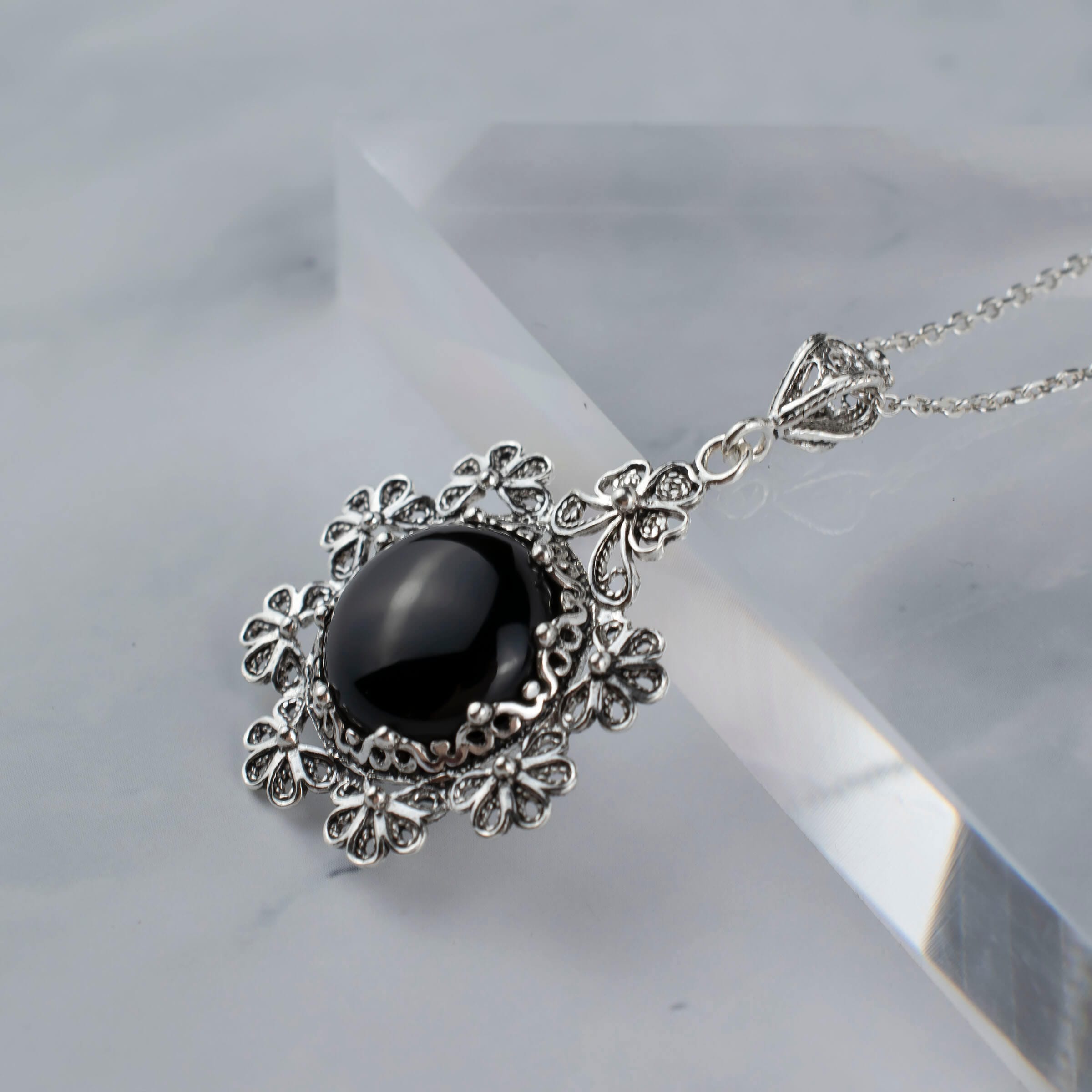 Sterling silver floral pendant featuring a black onyx gemstone, showcasing intricate filigree art design.