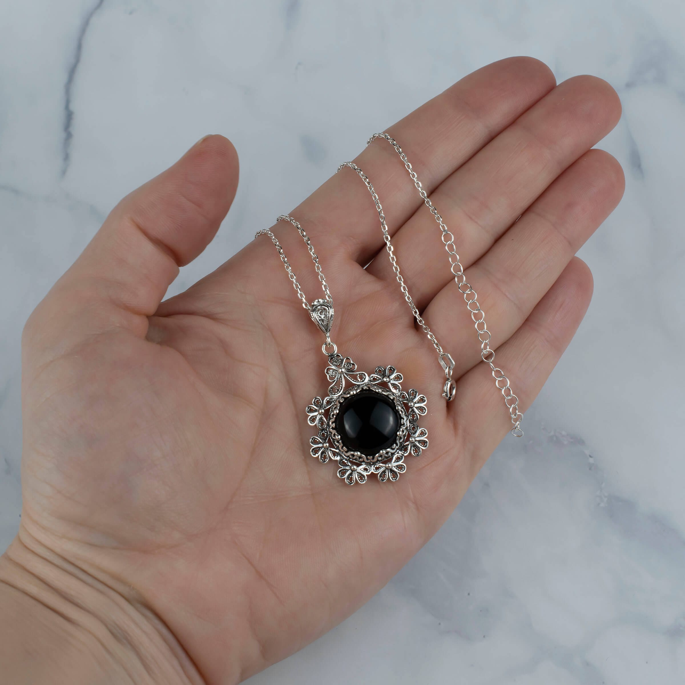 Sterling silver floral pendant featuring a black onyx gemstone, showcasing intricate filigree art design.