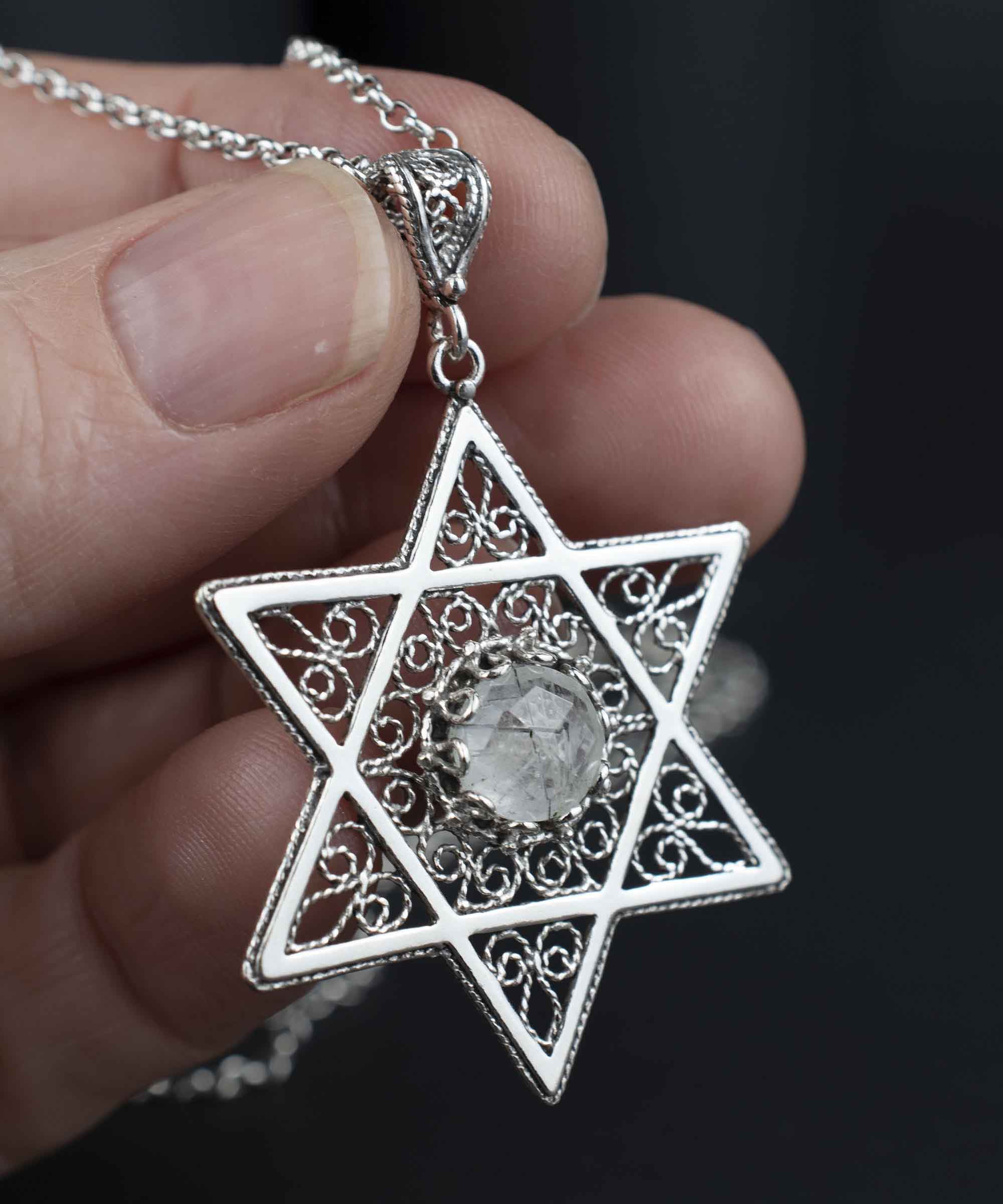 Handcrafted silver pendant featuring a black rutile gemstone in the shape of the Star of David, showcasing intricate filigree art.