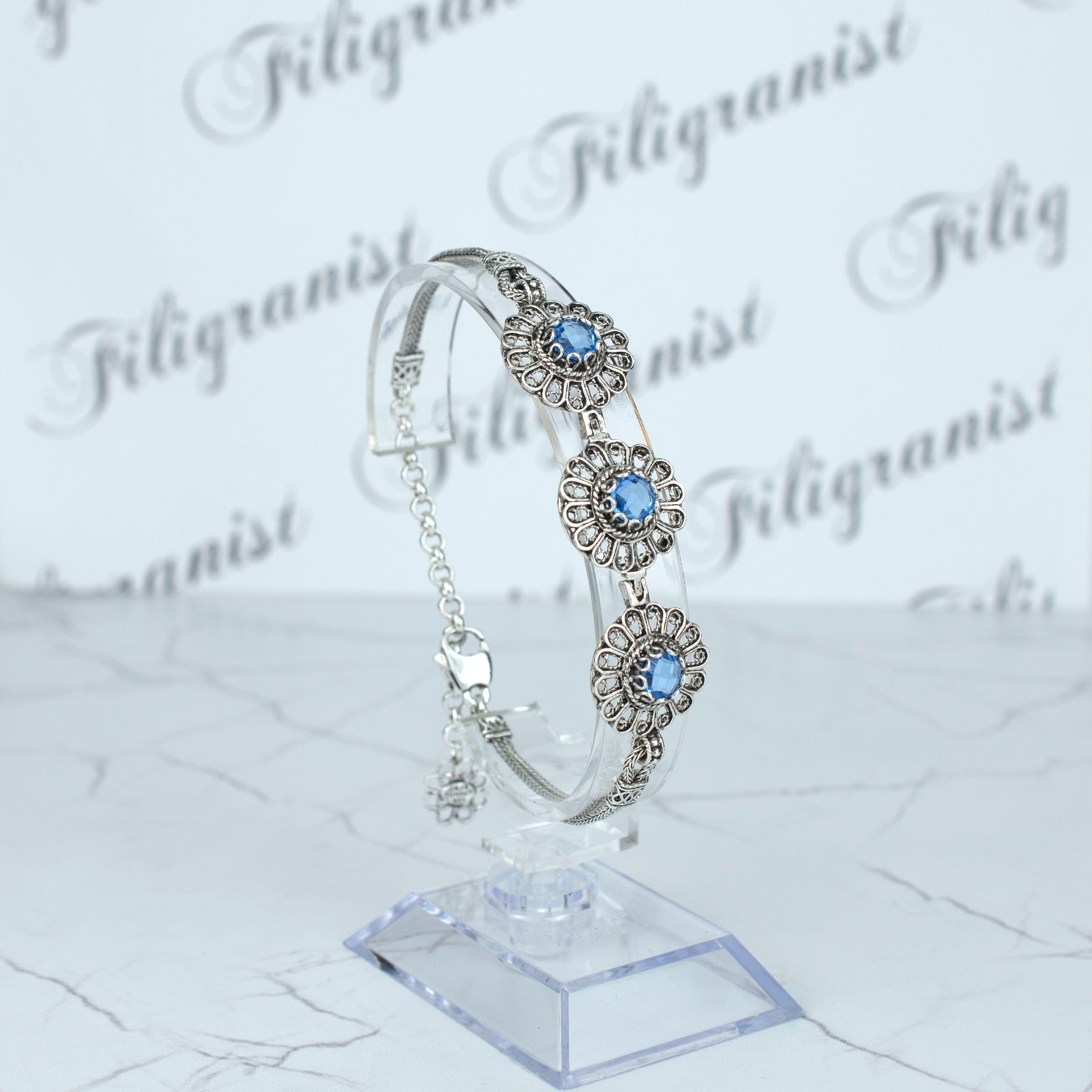 Elegant sterling silver link bracelet featuring intricate filigree art and a double-sided faceted blue quartz gemstone.