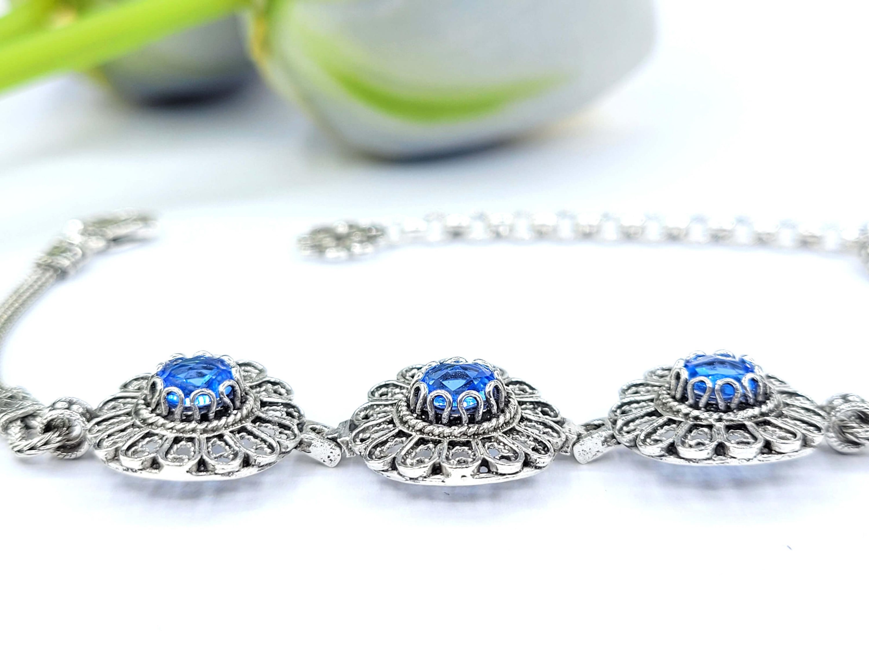 Elegant sterling silver link bracelet featuring intricate filigree art and a double-sided faceted blue quartz gemstone.