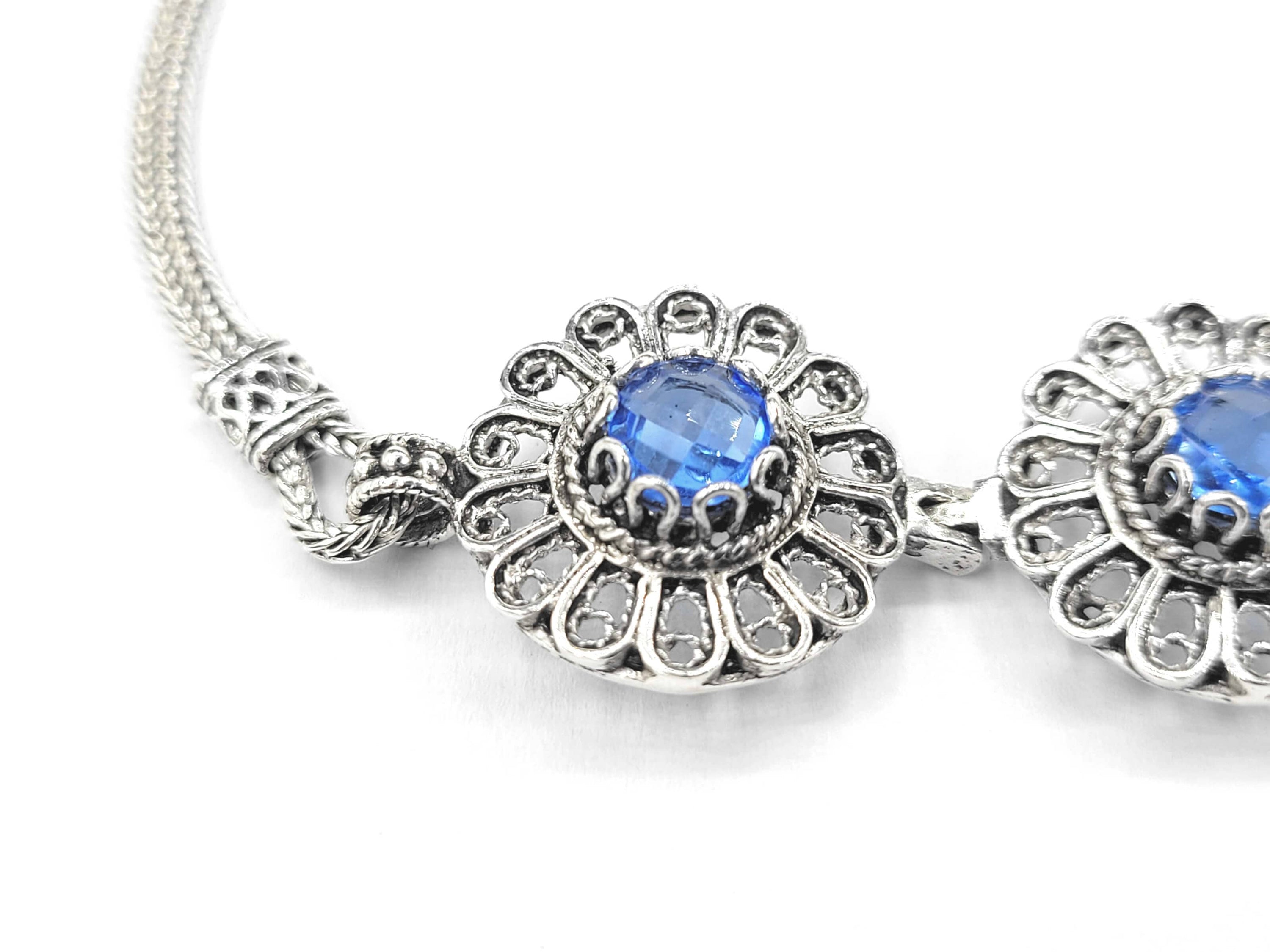 Elegant sterling silver link bracelet featuring intricate filigree art and a double-sided faceted blue quartz gemstone.