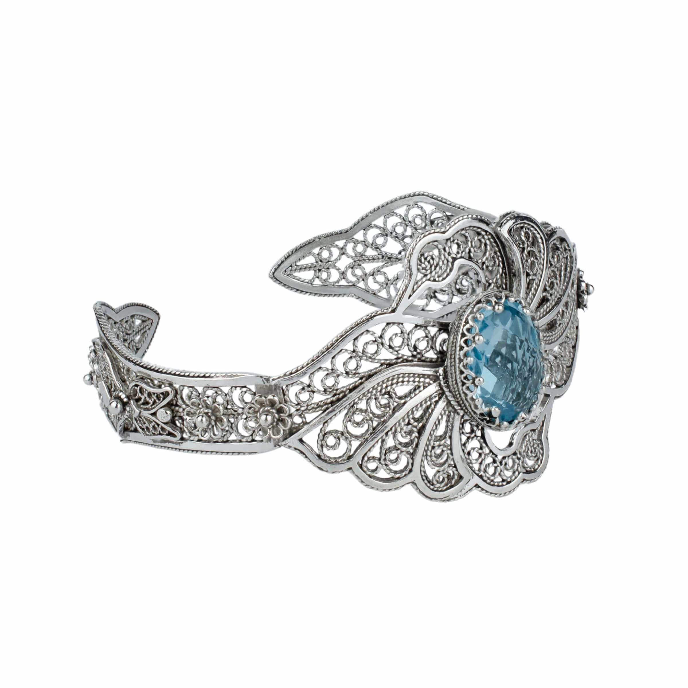 Elegant sterling silver cuff bracelet featuring intricate filigree design and a stunning blue topaz gemstone, shaped like double swans.