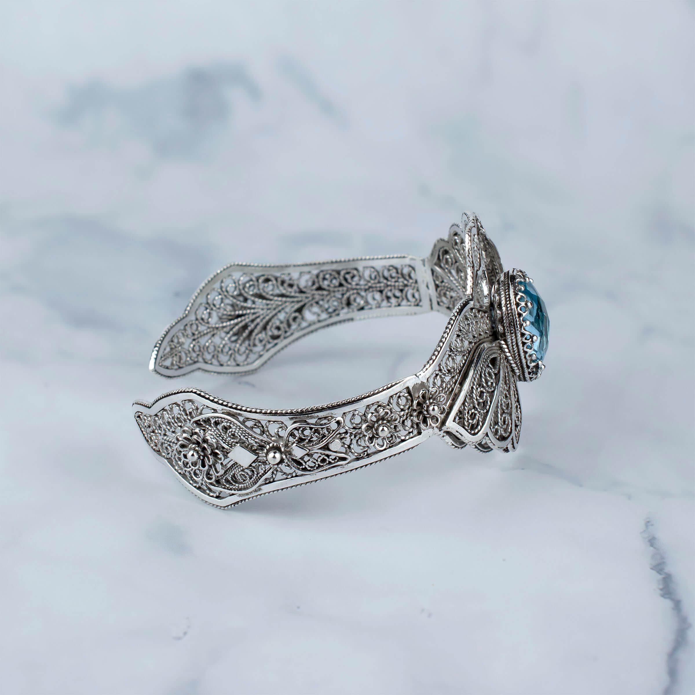 Elegant sterling silver cuff bracelet featuring intricate filigree design and a stunning blue topaz gemstone, shaped like double swans.