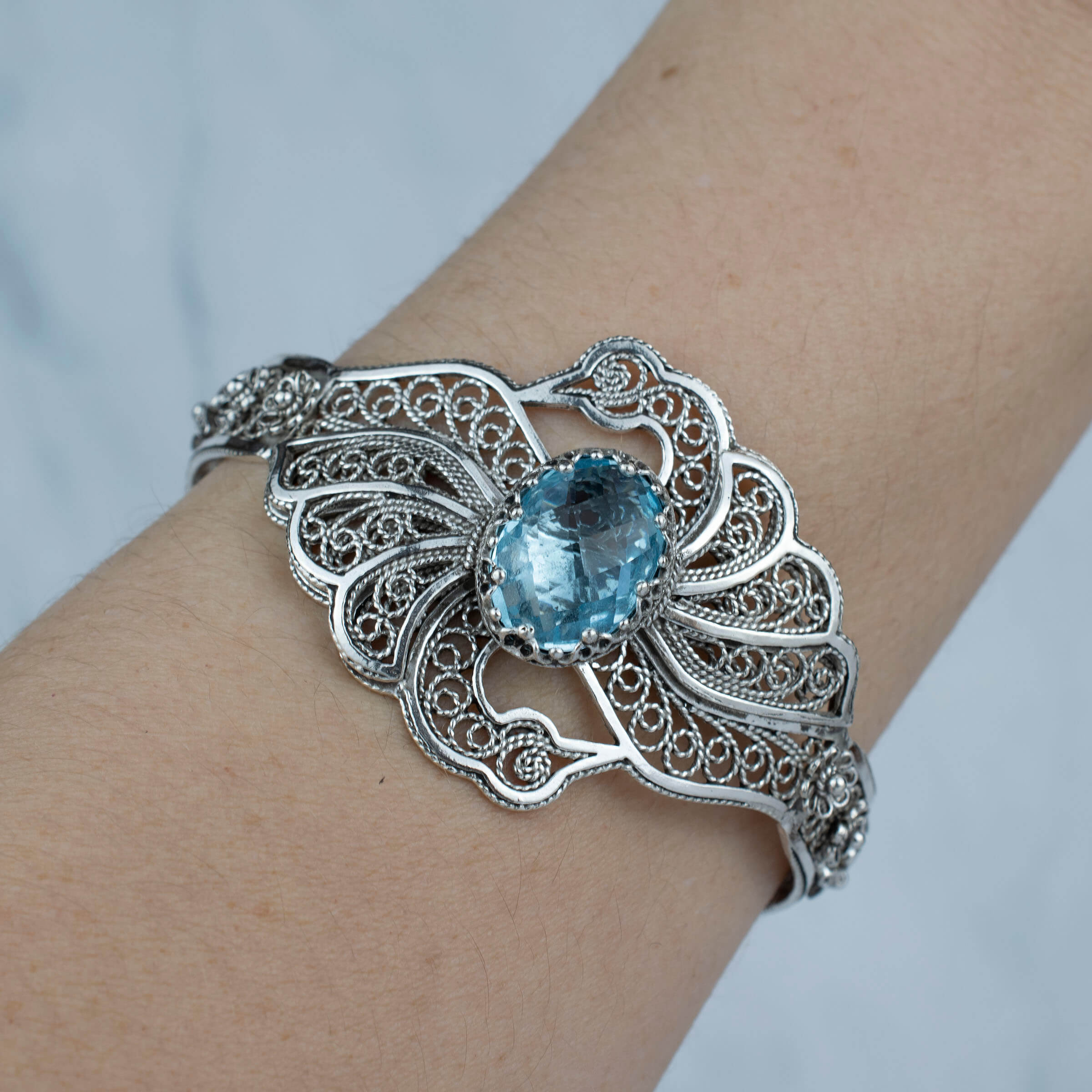 Elegant sterling silver cuff bracelet featuring intricate filigree design and a stunning blue topaz gemstone, shaped like double swans.