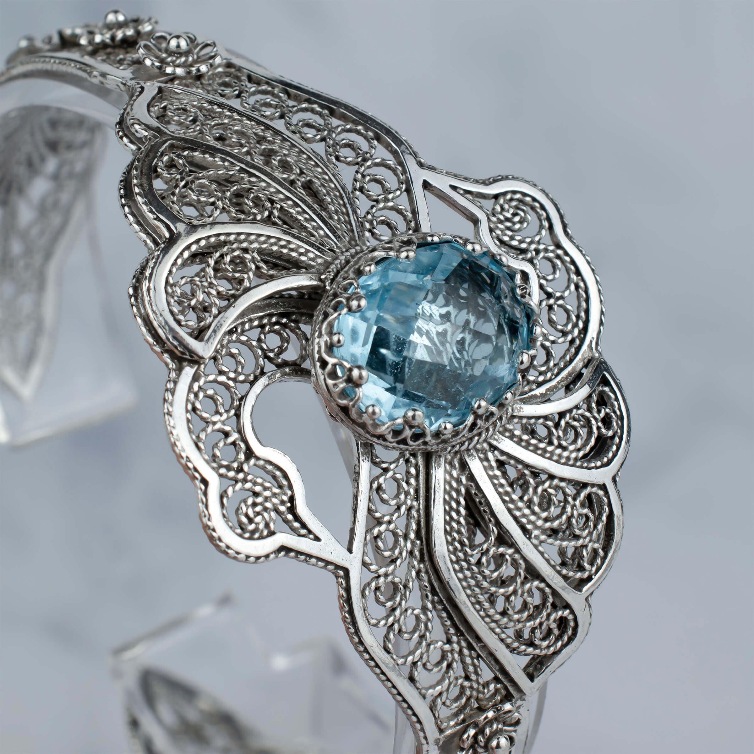 Elegant sterling silver cuff bracelet featuring intricate filigree design and a stunning blue topaz gemstone, shaped like double swans.