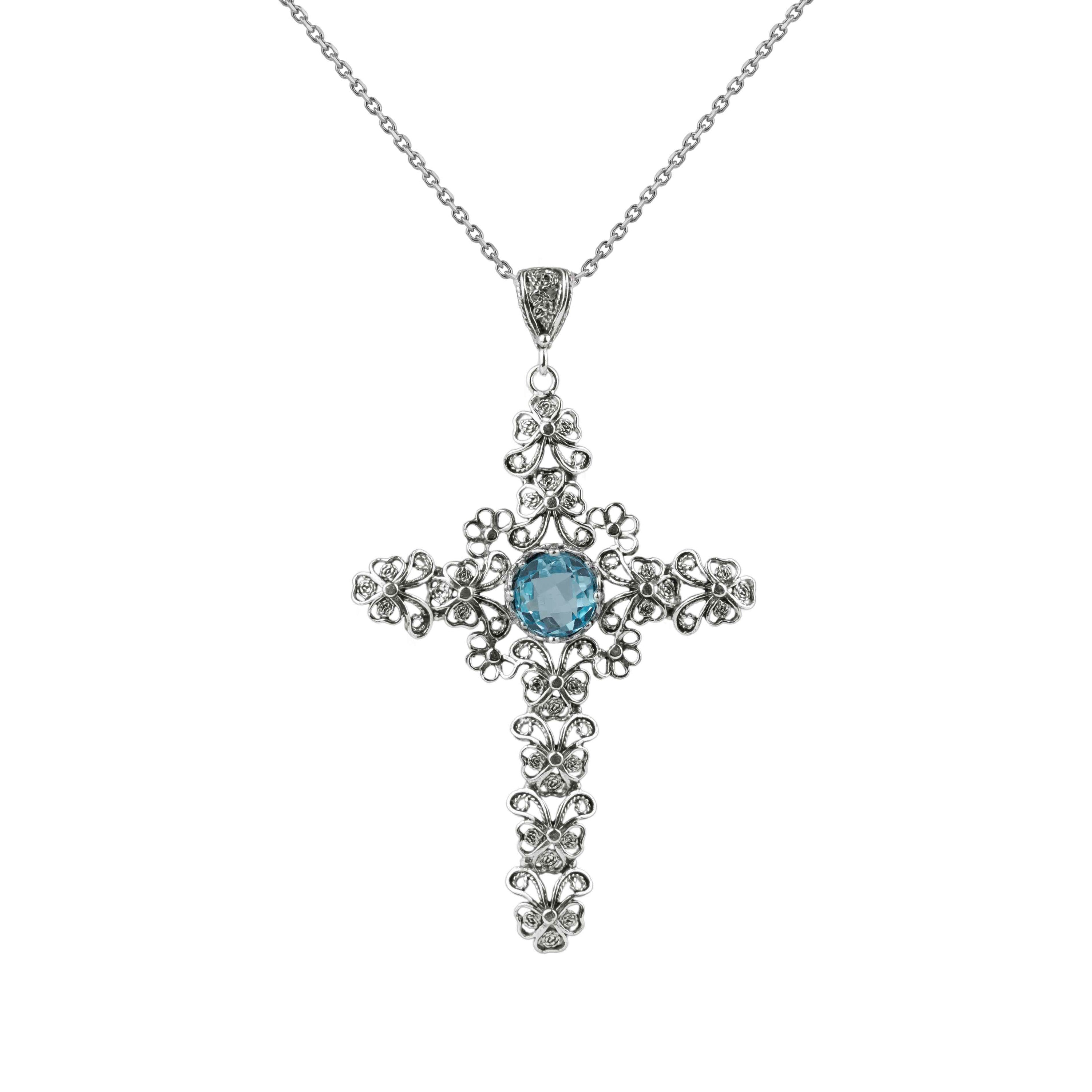 Handcrafted silver pendant featuring a blue topaz gemstone in a unique cross design, showcasing intricate filigree art.