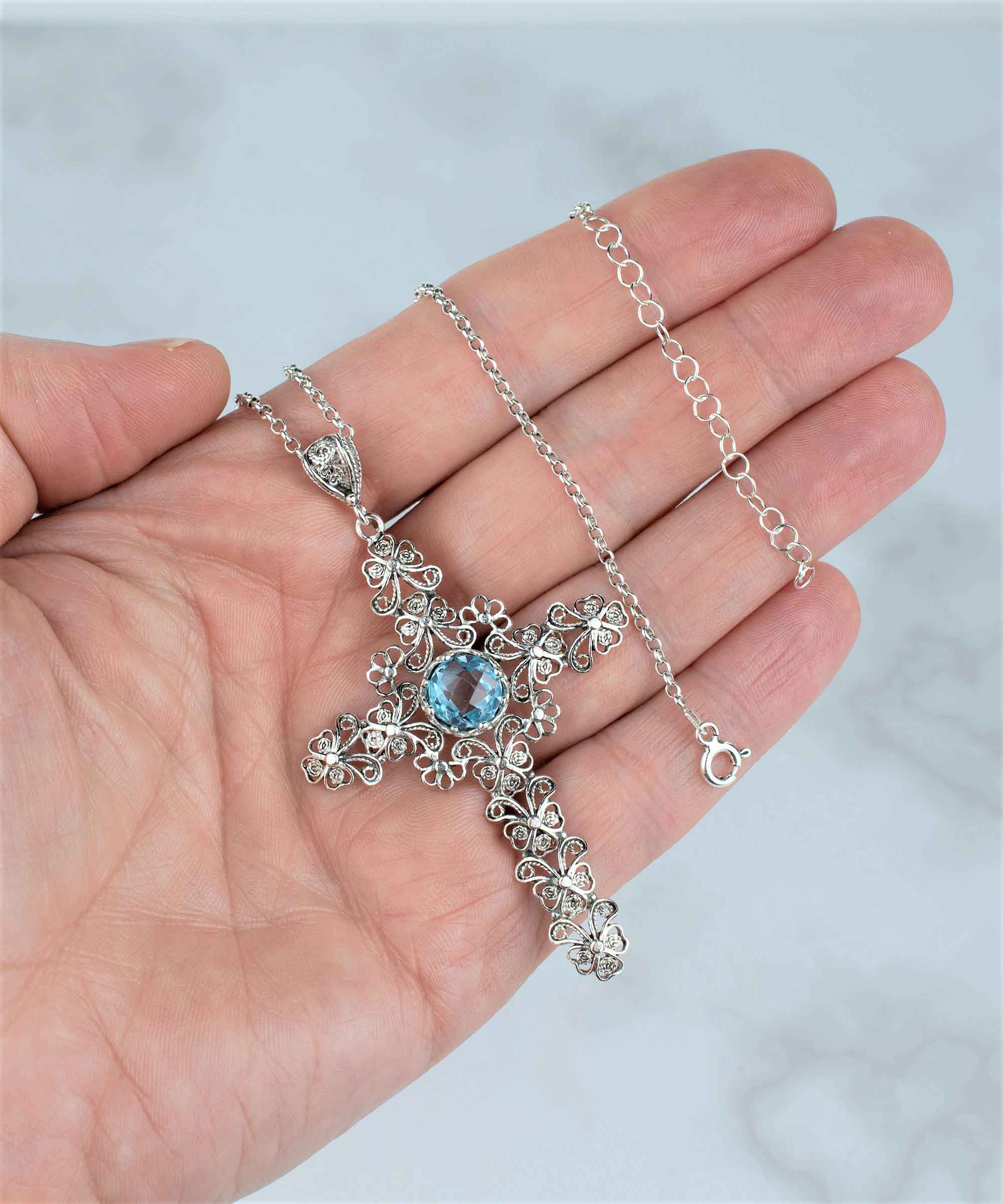 Handcrafted silver pendant featuring a blue topaz gemstone in a unique cross design, showcasing intricate filigree art.