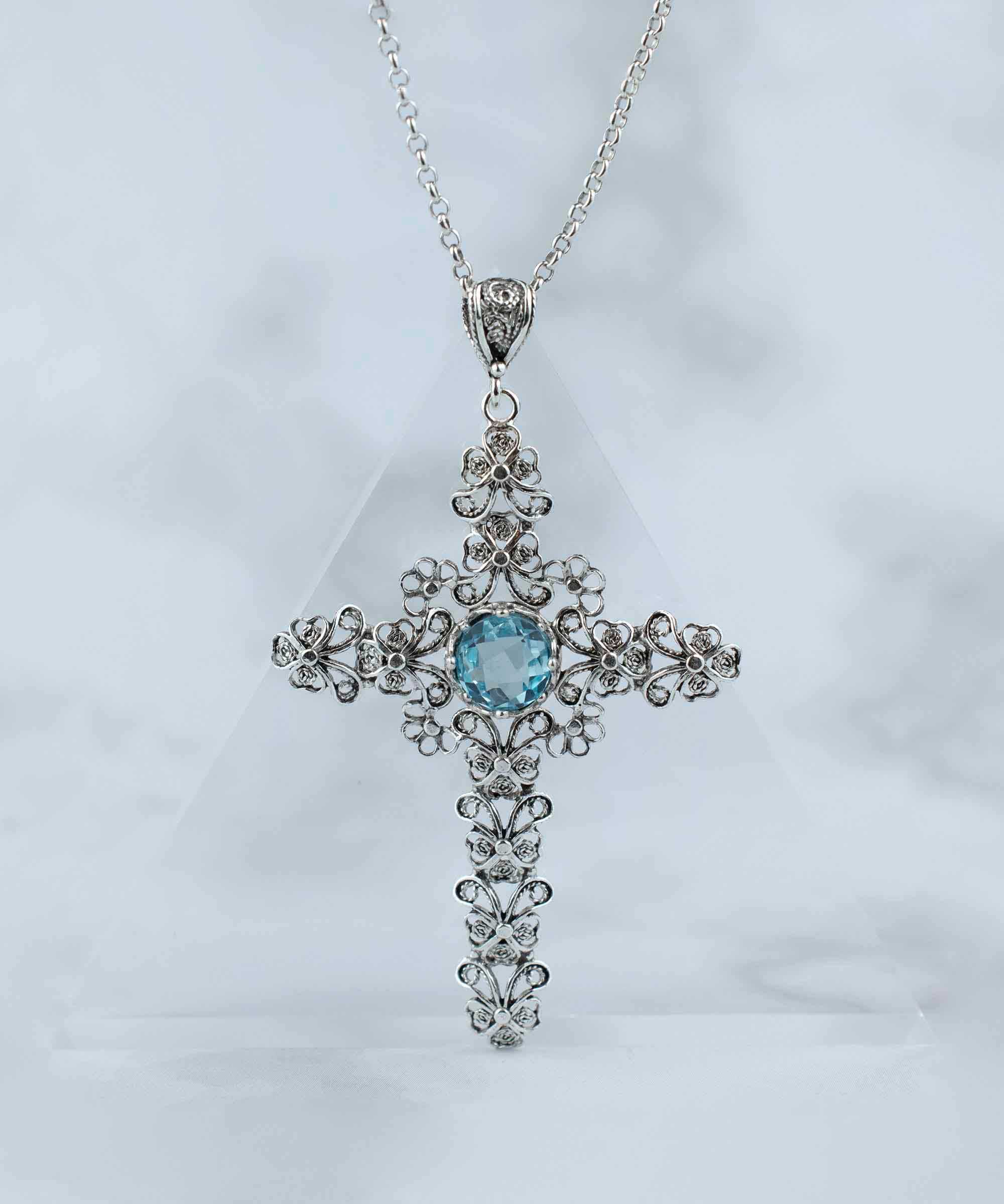 Handcrafted silver pendant featuring a blue topaz gemstone in a unique cross design, showcasing intricate filigree art.