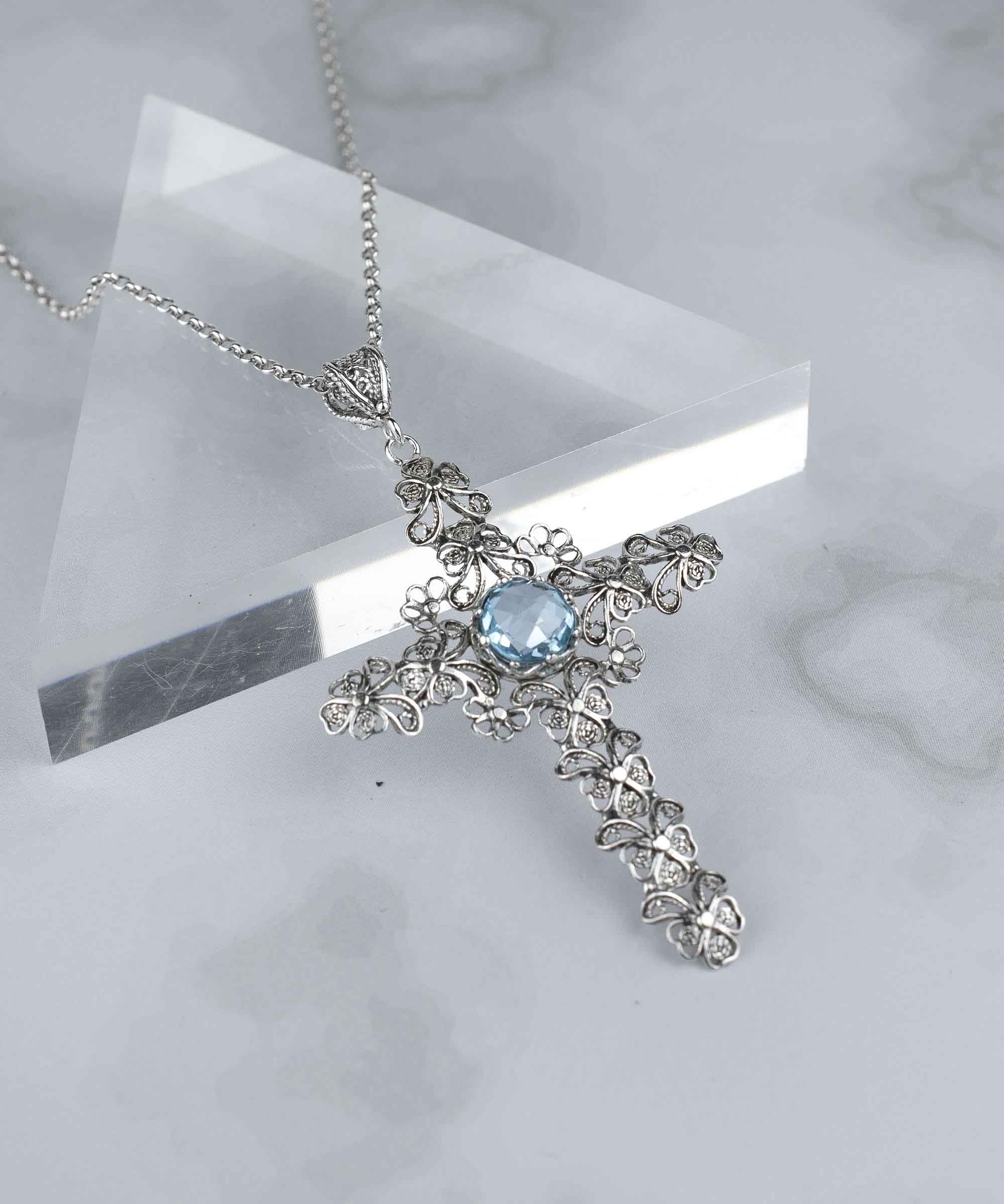 Handcrafted silver pendant featuring a blue topaz gemstone in a unique cross design, showcasing intricate filigree art.