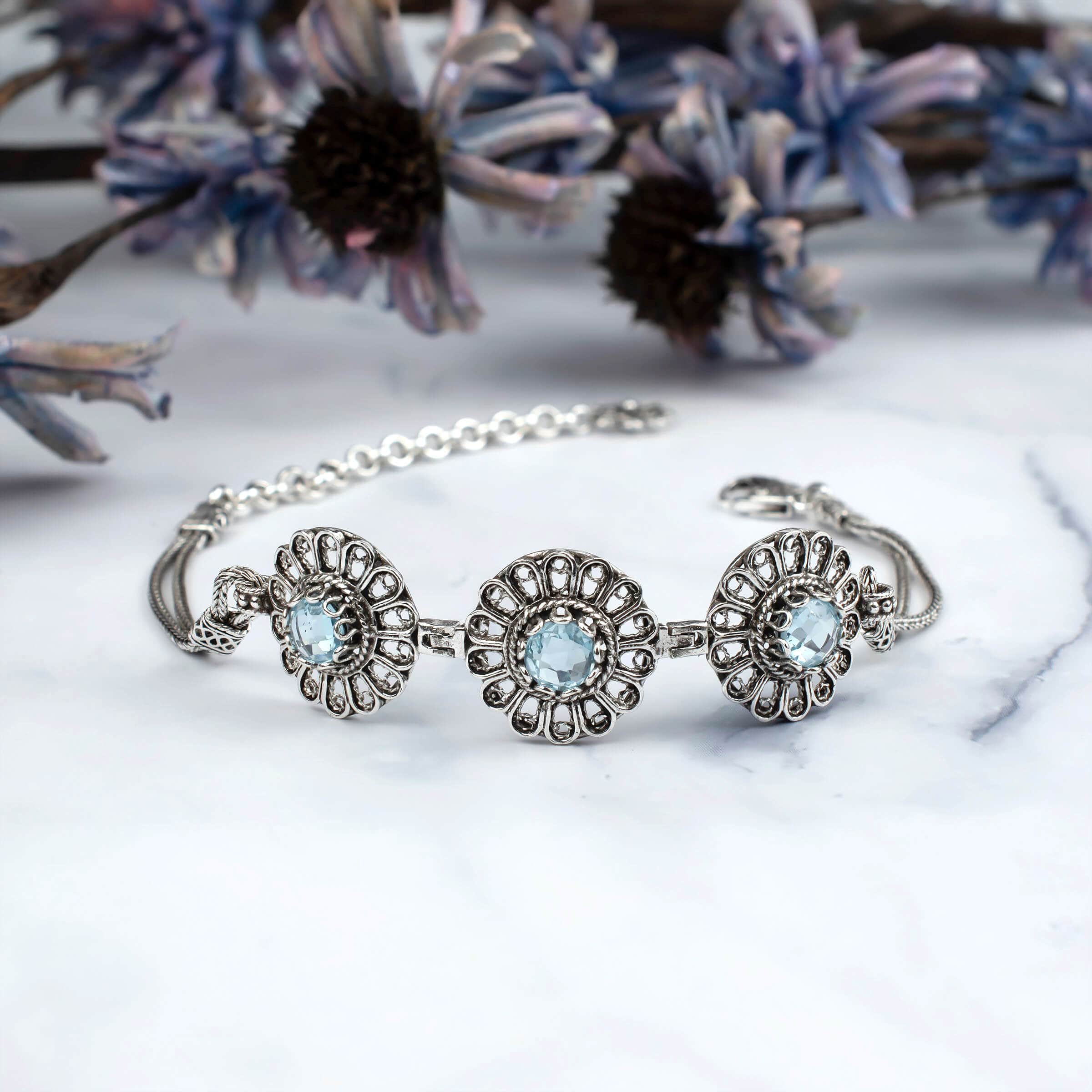 Elegant sterling silver link bracelet featuring intricate filigree art and a stunning sky blue topaz gemstone centerpiece.