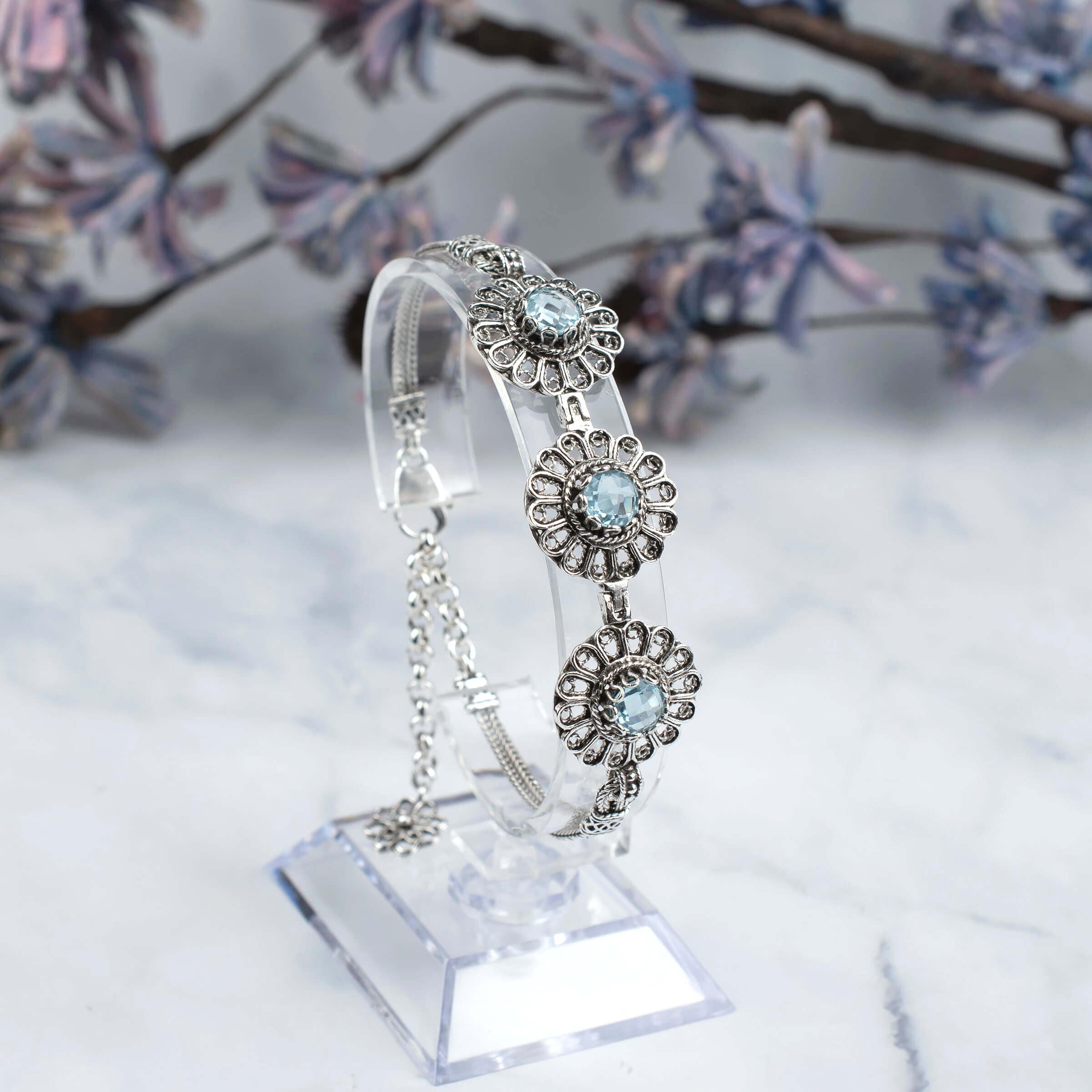 Elegant sterling silver link bracelet featuring intricate filigree art and a stunning sky blue topaz gemstone centerpiece.