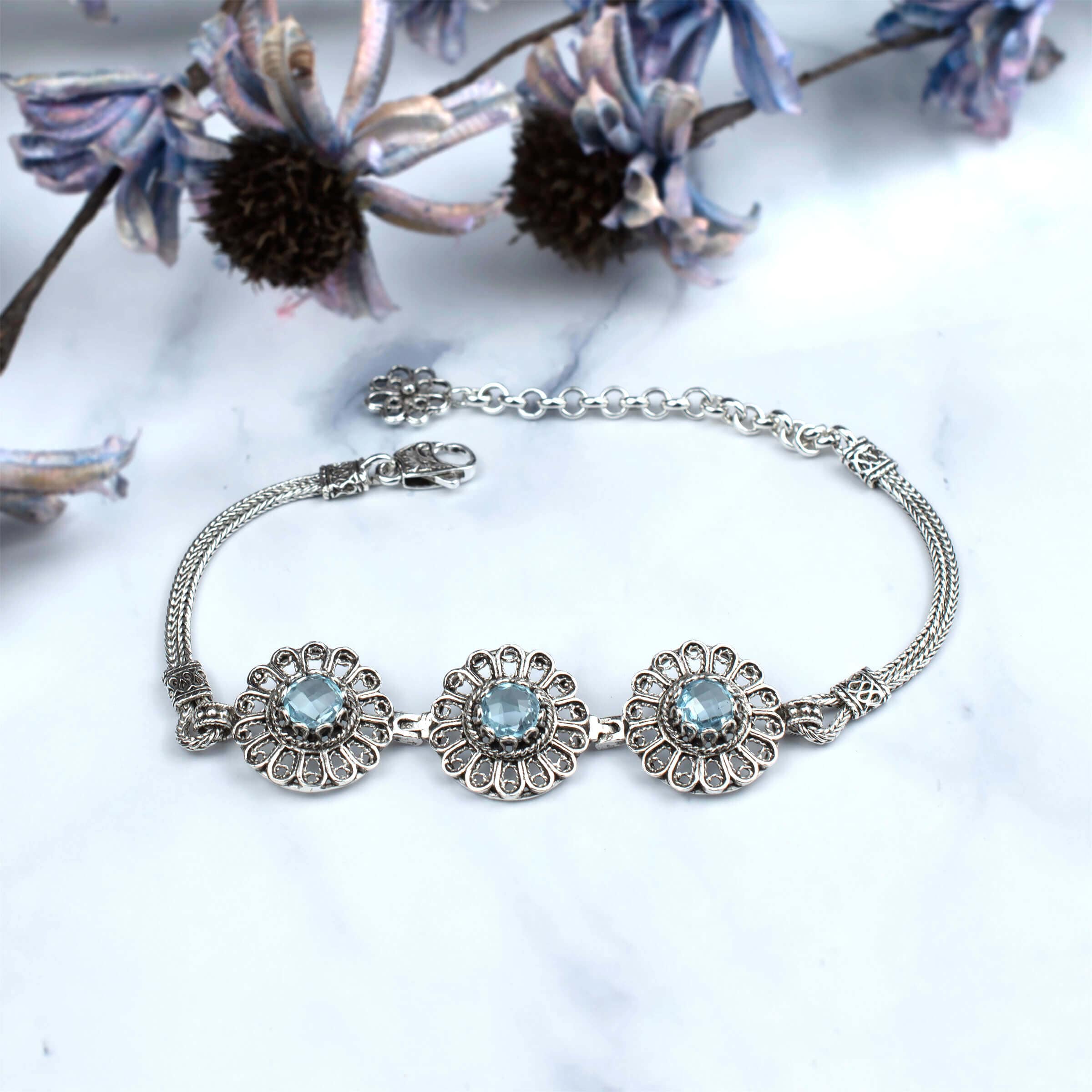 Elegant sterling silver link bracelet featuring intricate filigree art and a stunning sky blue topaz gemstone centerpiece.