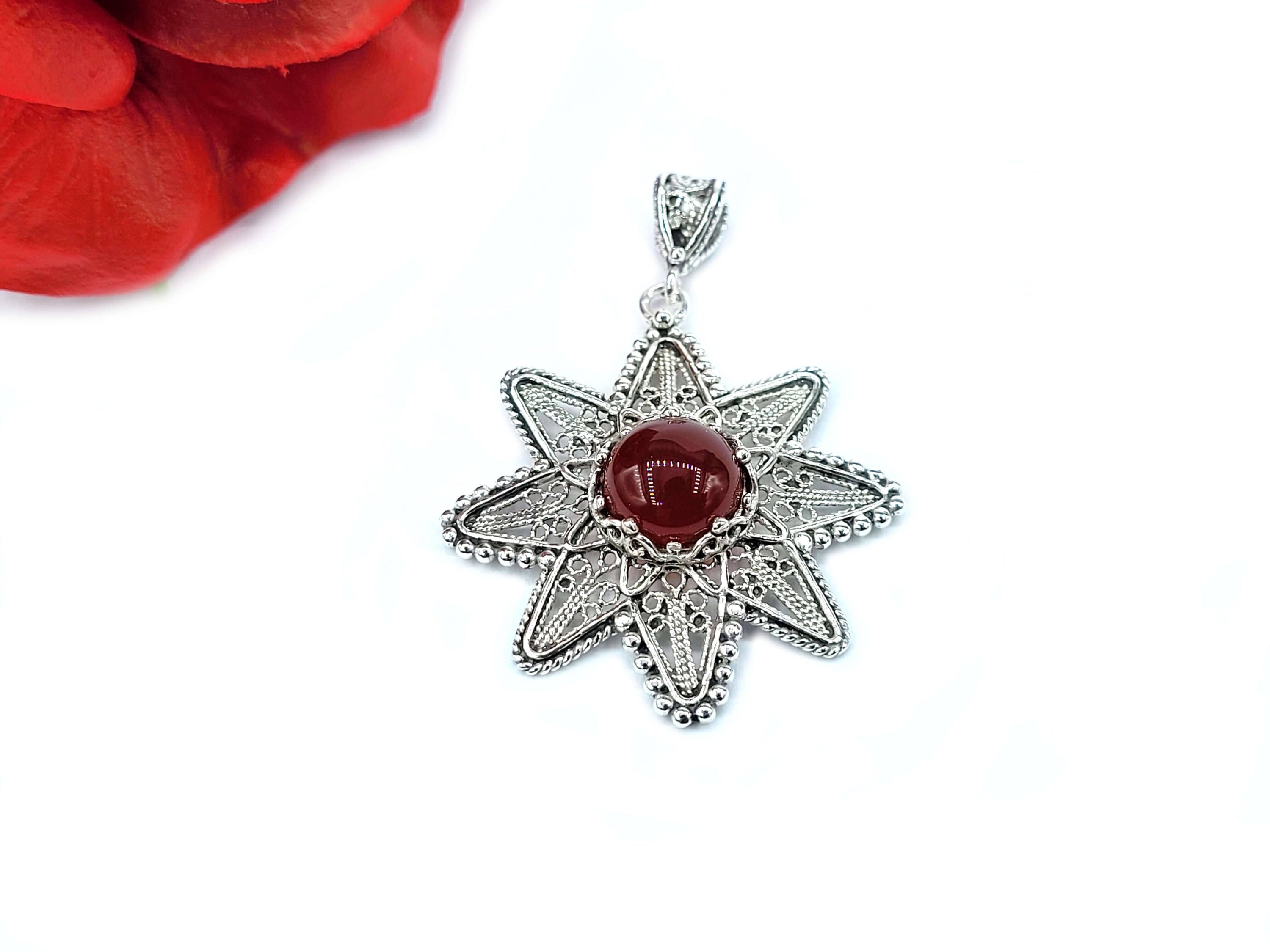 A stunning silver pendant featuring a sunflower design with a natural carnelian gemstone at the center, showcasing intricate filigree art.