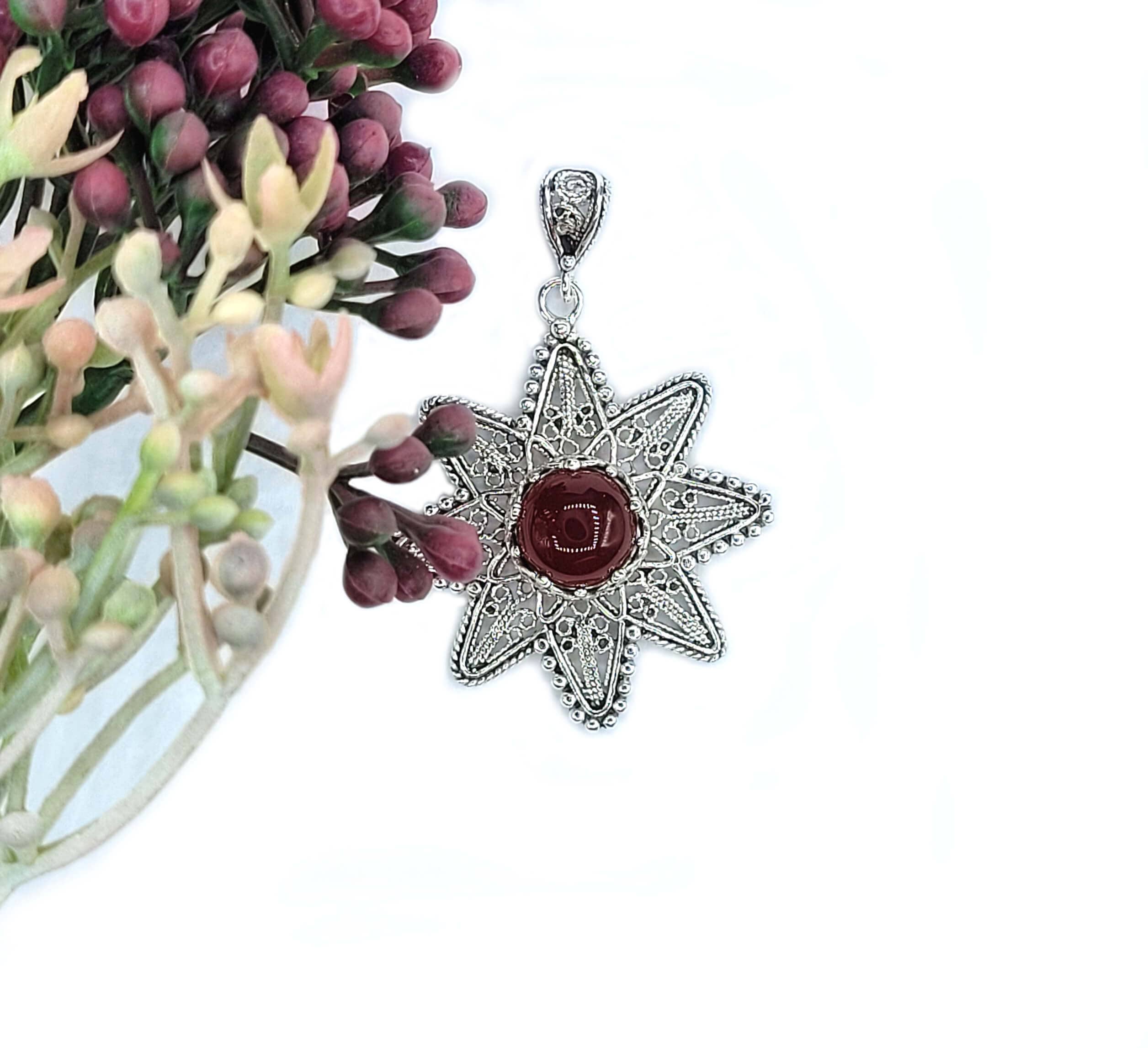 A stunning silver pendant featuring a sunflower design with a natural carnelian gemstone at the center, showcasing intricate filigree art.