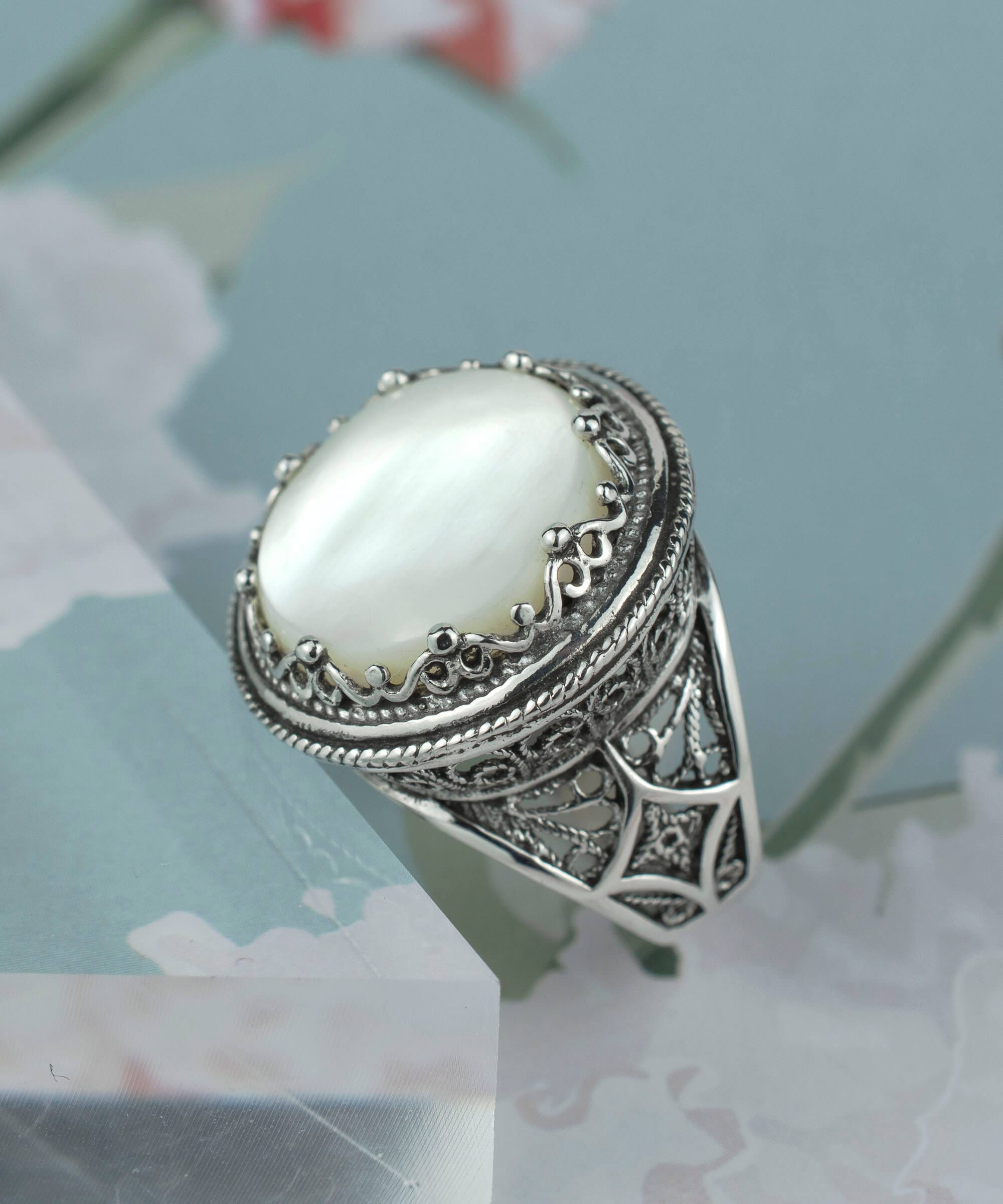 A stunning sterling silver ring featuring a round mother of pearl gemstone with intricate filigree design, perfect for bold statement wear.