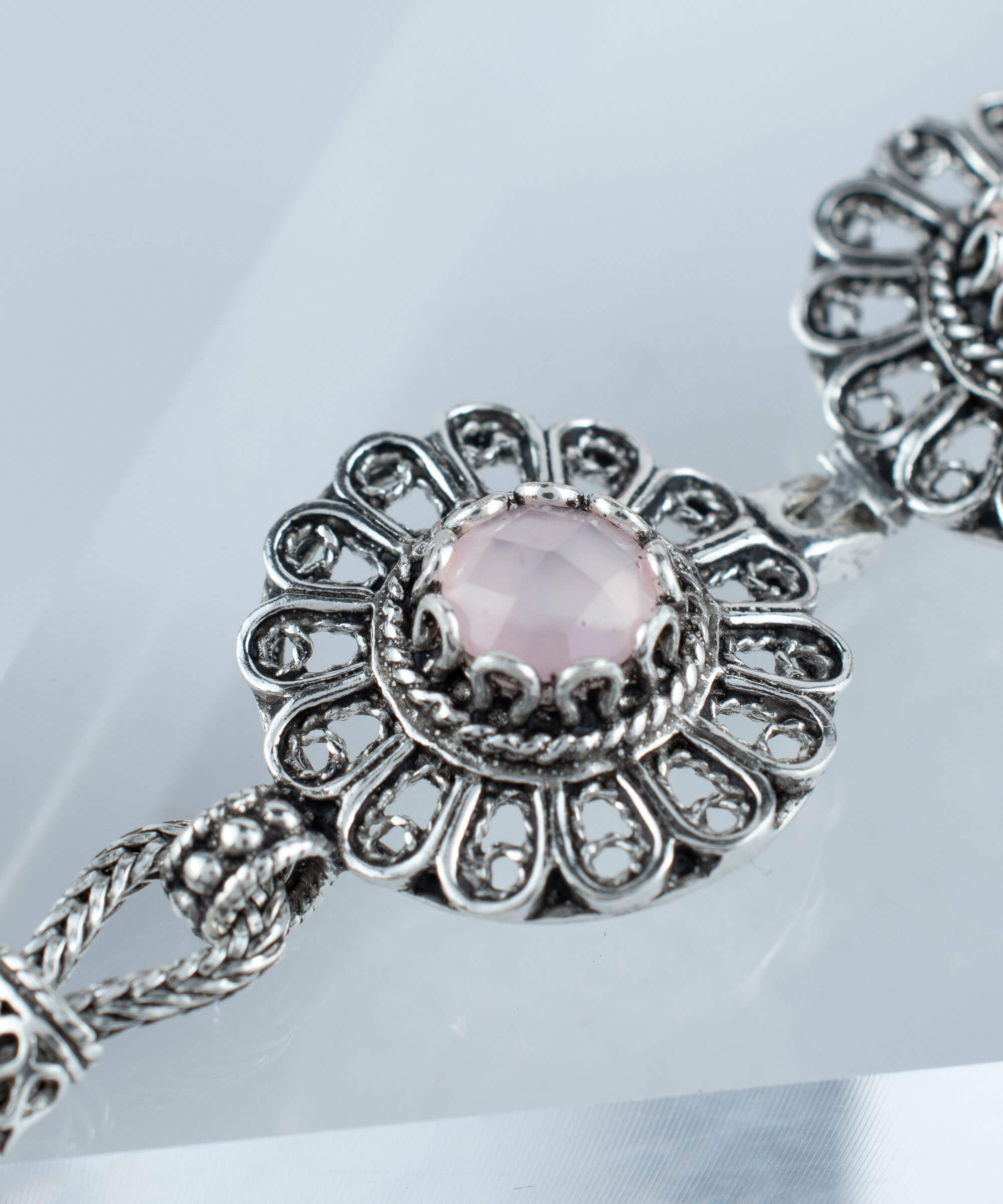 Elegant sterling silver link bracelet featuring intricate filigree art and a double-sided faceted pink chalcedony gemstone.