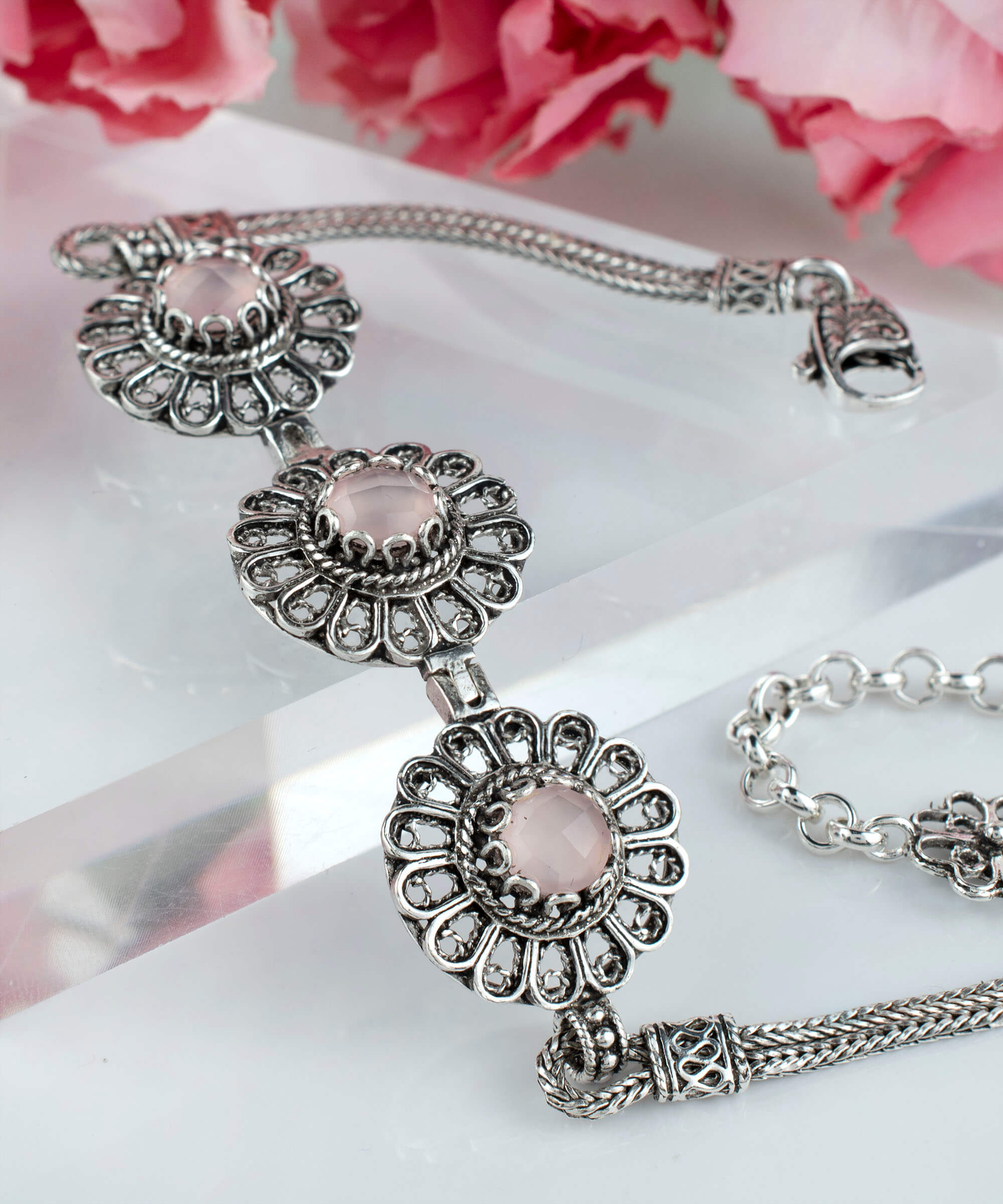 Elegant sterling silver link bracelet featuring intricate filigree art and a double-sided faceted pink chalcedony gemstone.