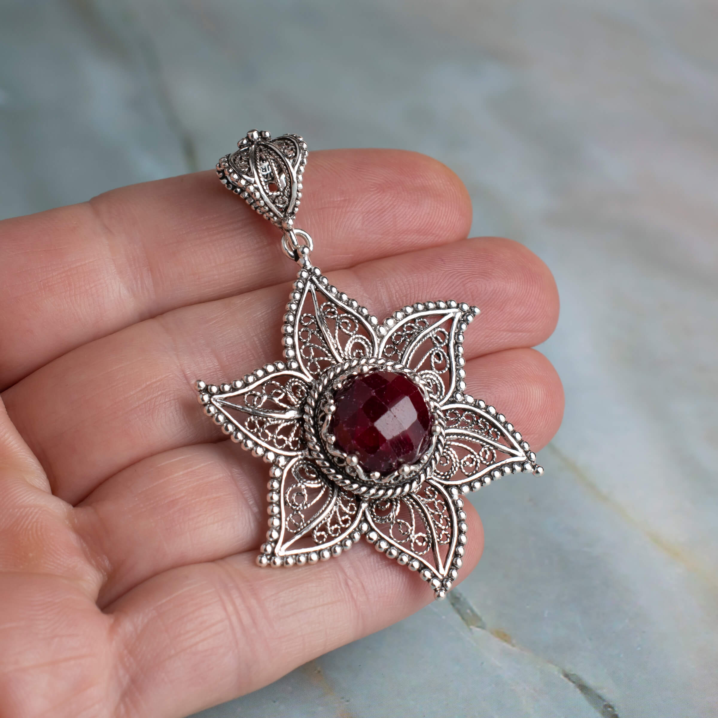 Elegant sterling silver pendant featuring a ruby corundum gemstone in a star design with intricate filigree art.