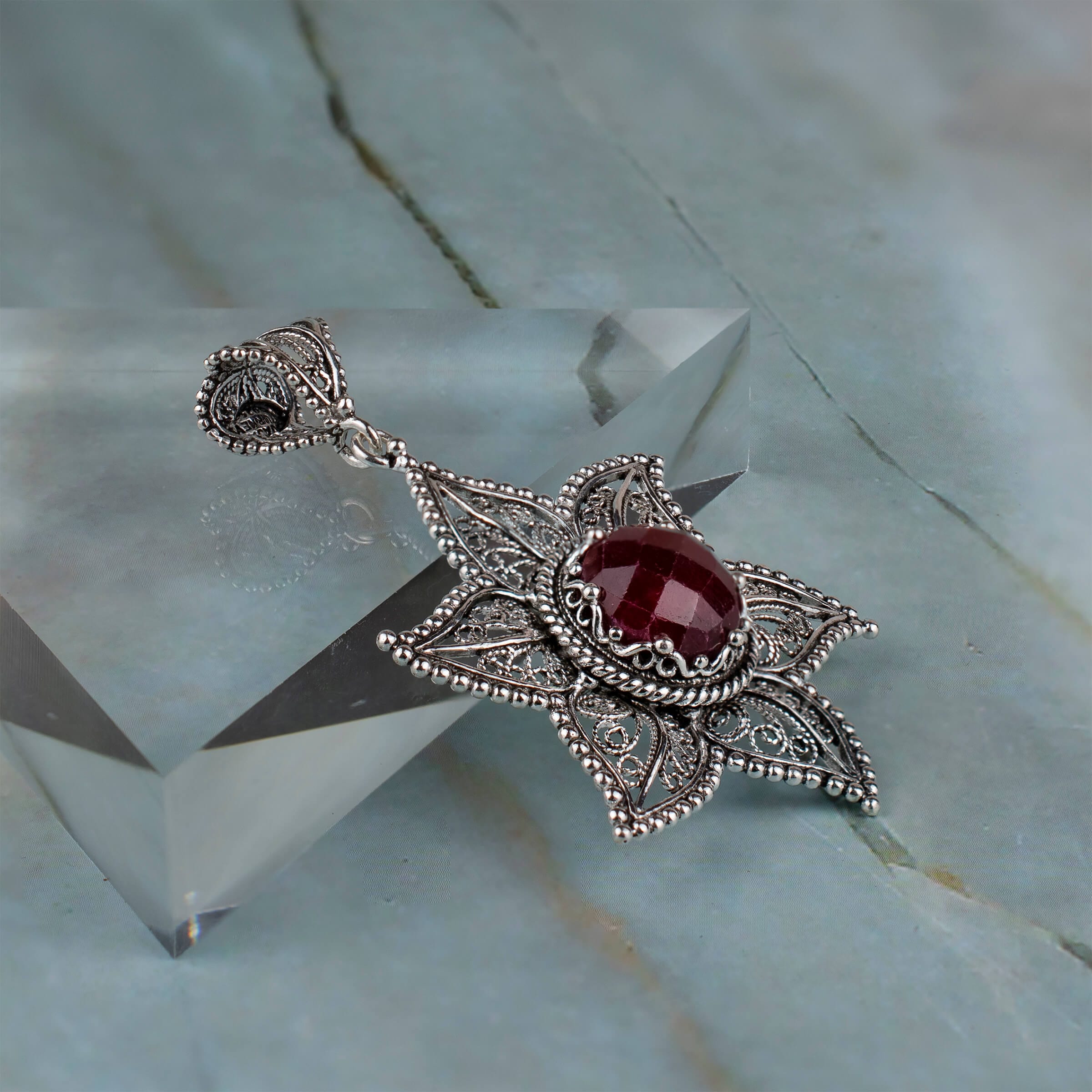 Elegant sterling silver pendant featuring a ruby corundum gemstone in a star design with intricate filigree art.