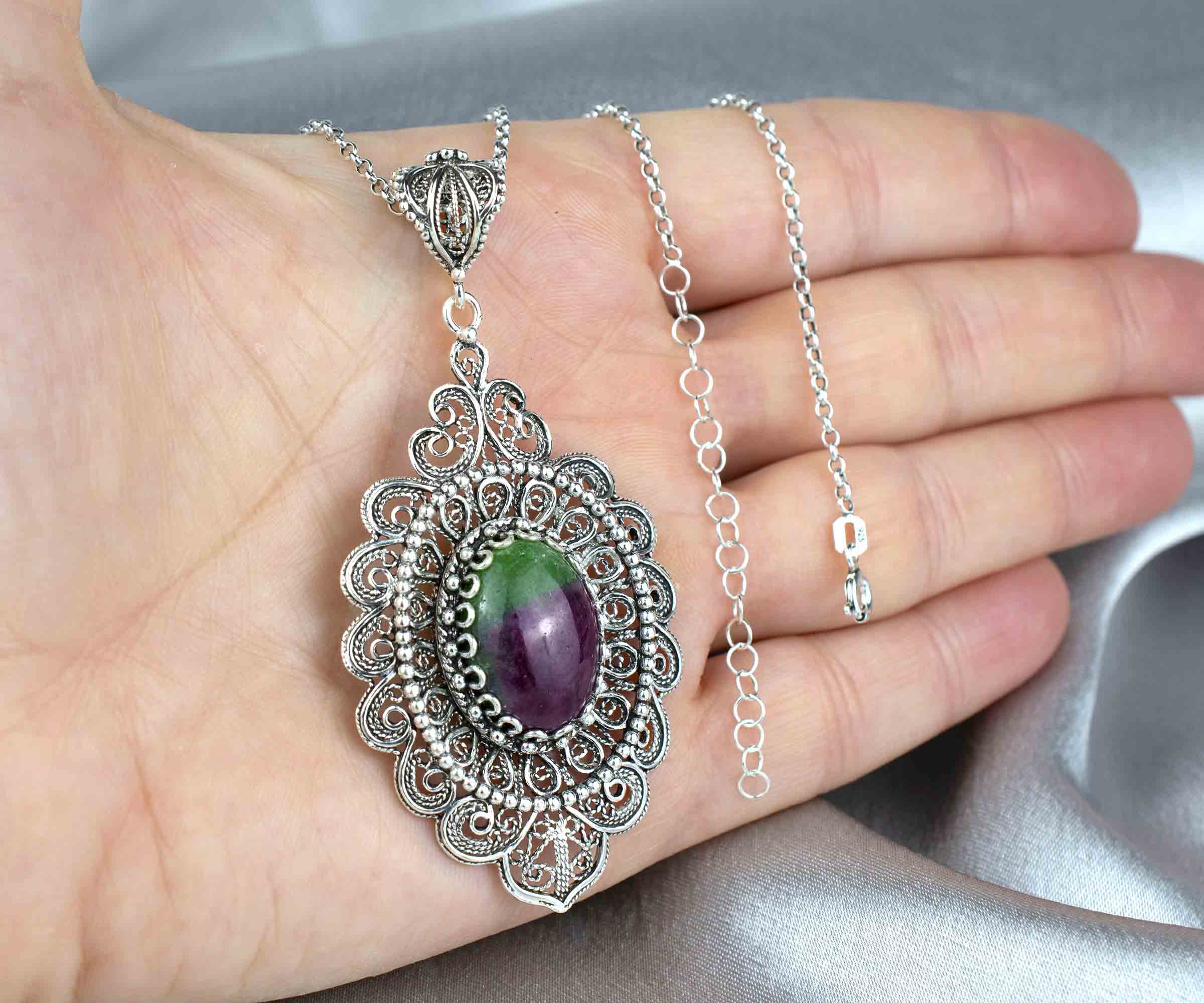 Elegant sterling silver pendant necklace featuring intricate filigree design and a vibrant ruby zoisite gemstone in an oval cut.