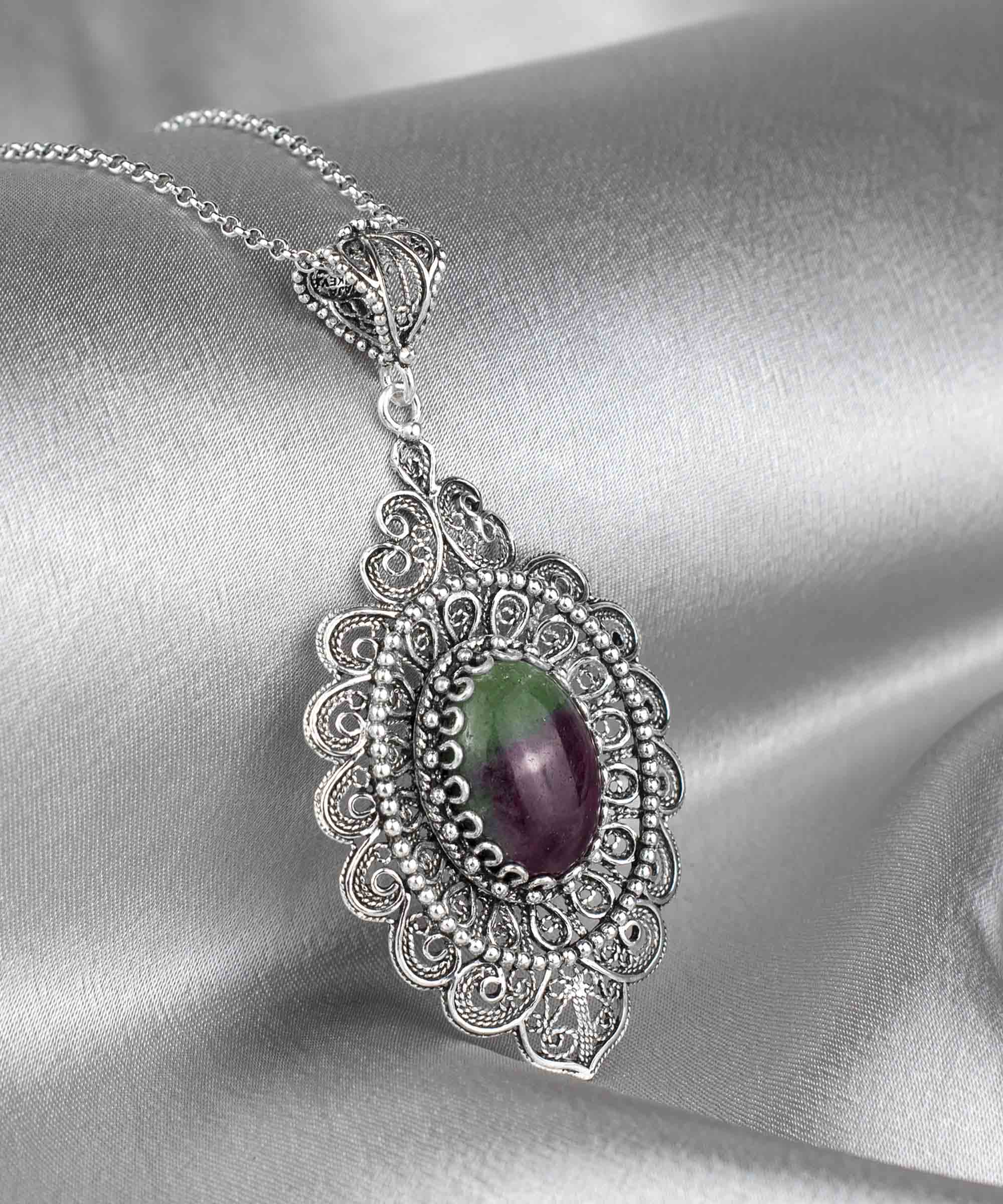 Elegant sterling silver pendant necklace featuring intricate filigree design and a vibrant ruby zoisite gemstone in an oval cut.