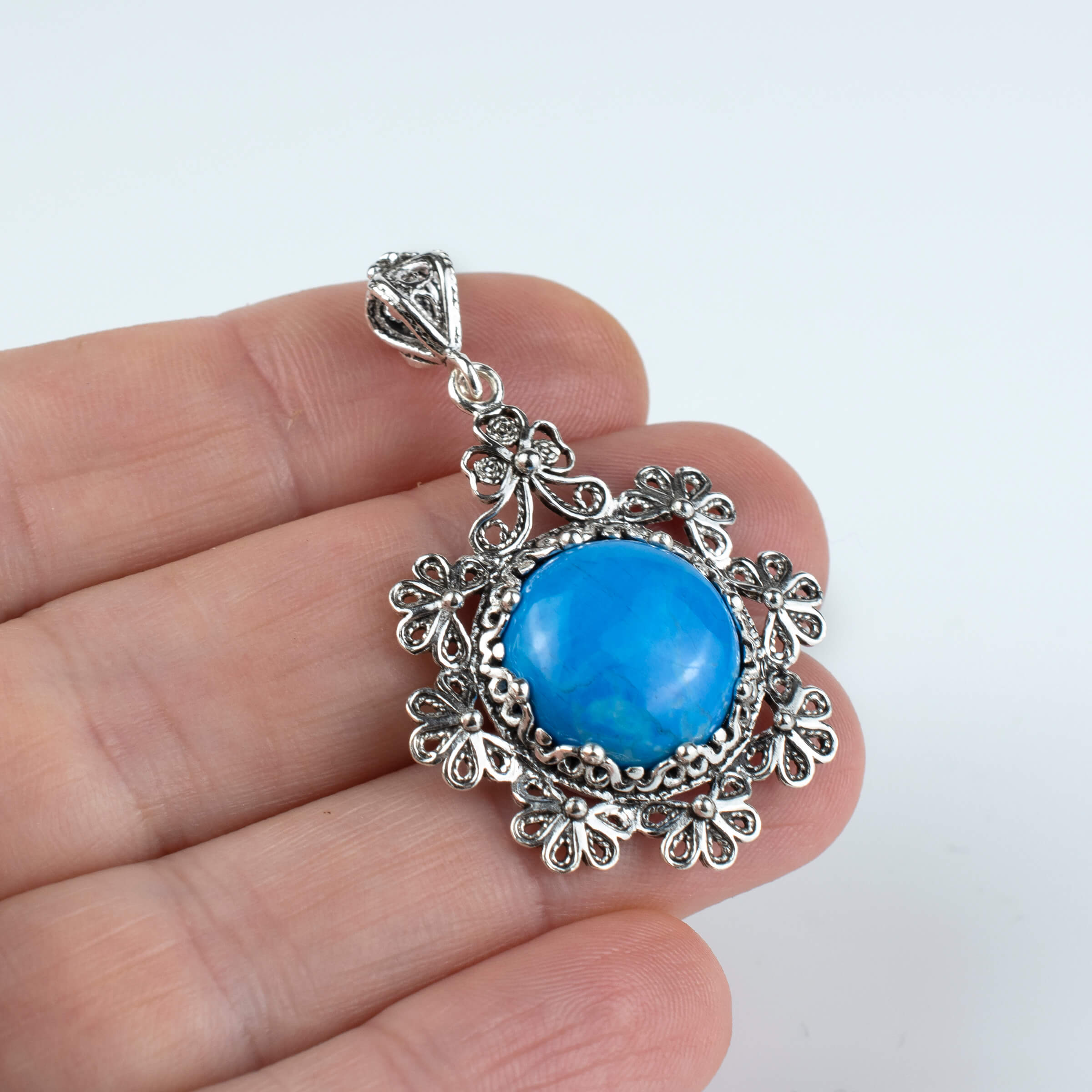 Sterling silver filigree pendant featuring a turquoise gemstone in a floral design, showcasing intricate craftsmanship.