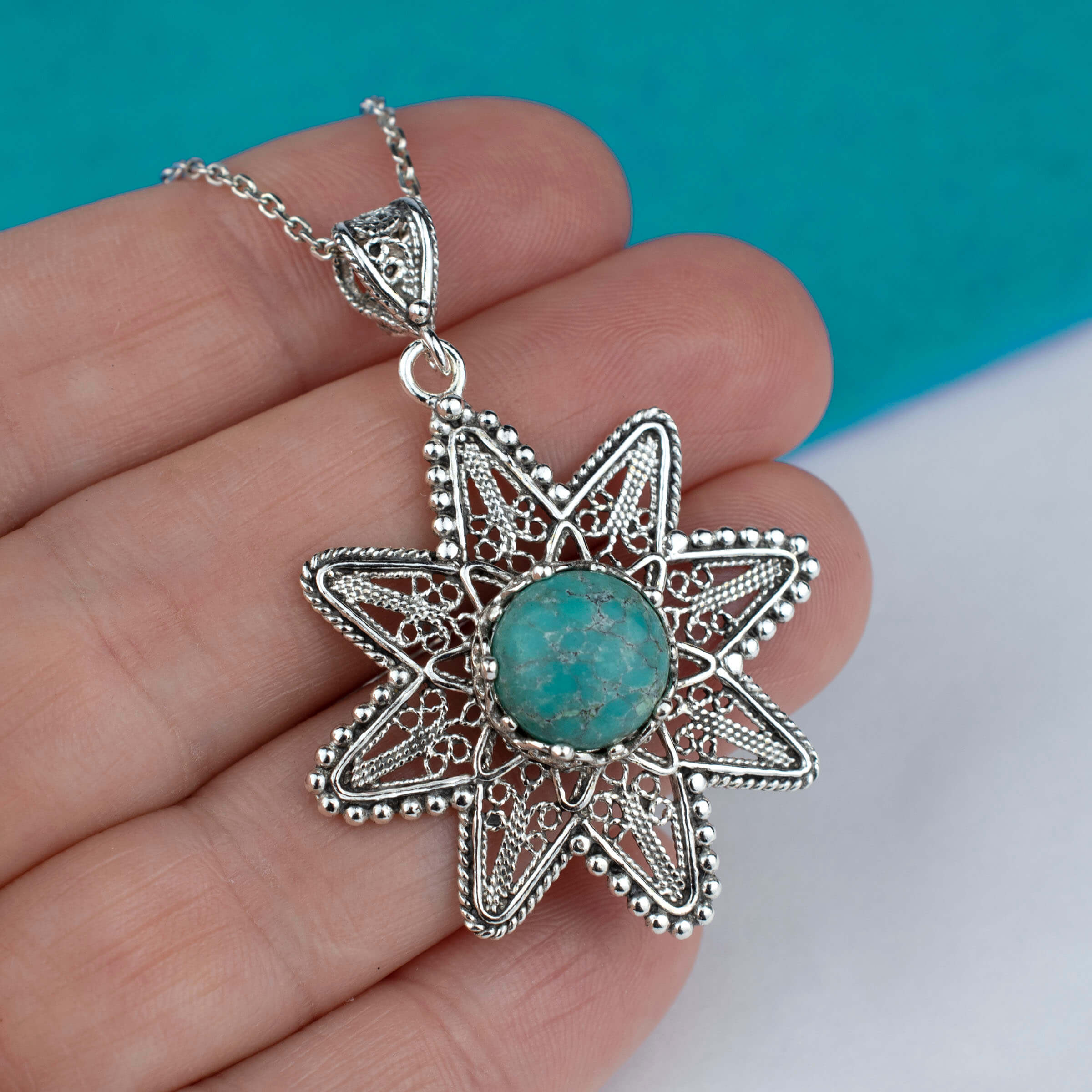 Sterling silver pendant featuring a turquoise gemstone in a sunflower design, showcasing intricate filigree art.