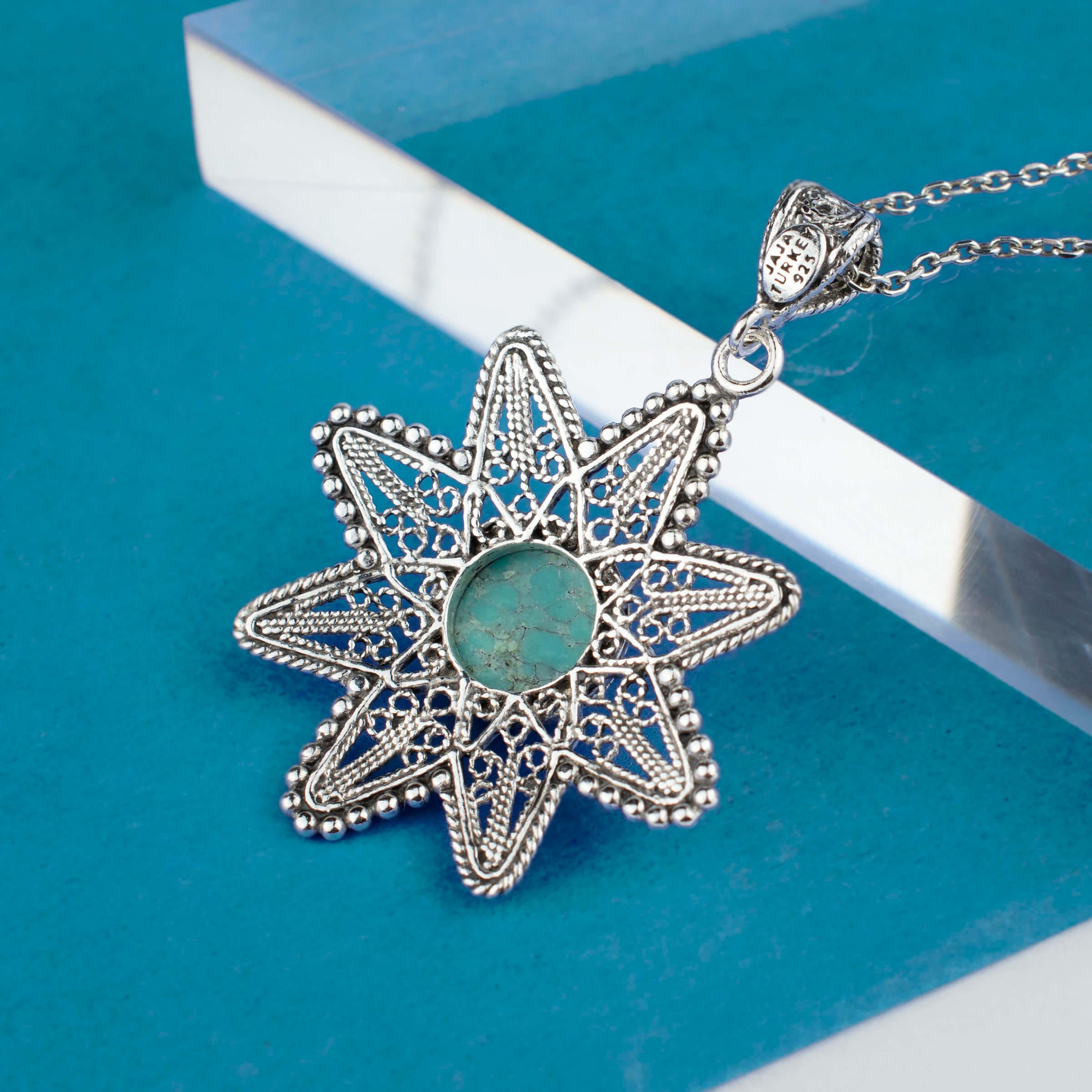 Sterling silver pendant featuring a turquoise gemstone in a sunflower design, showcasing intricate filigree art.