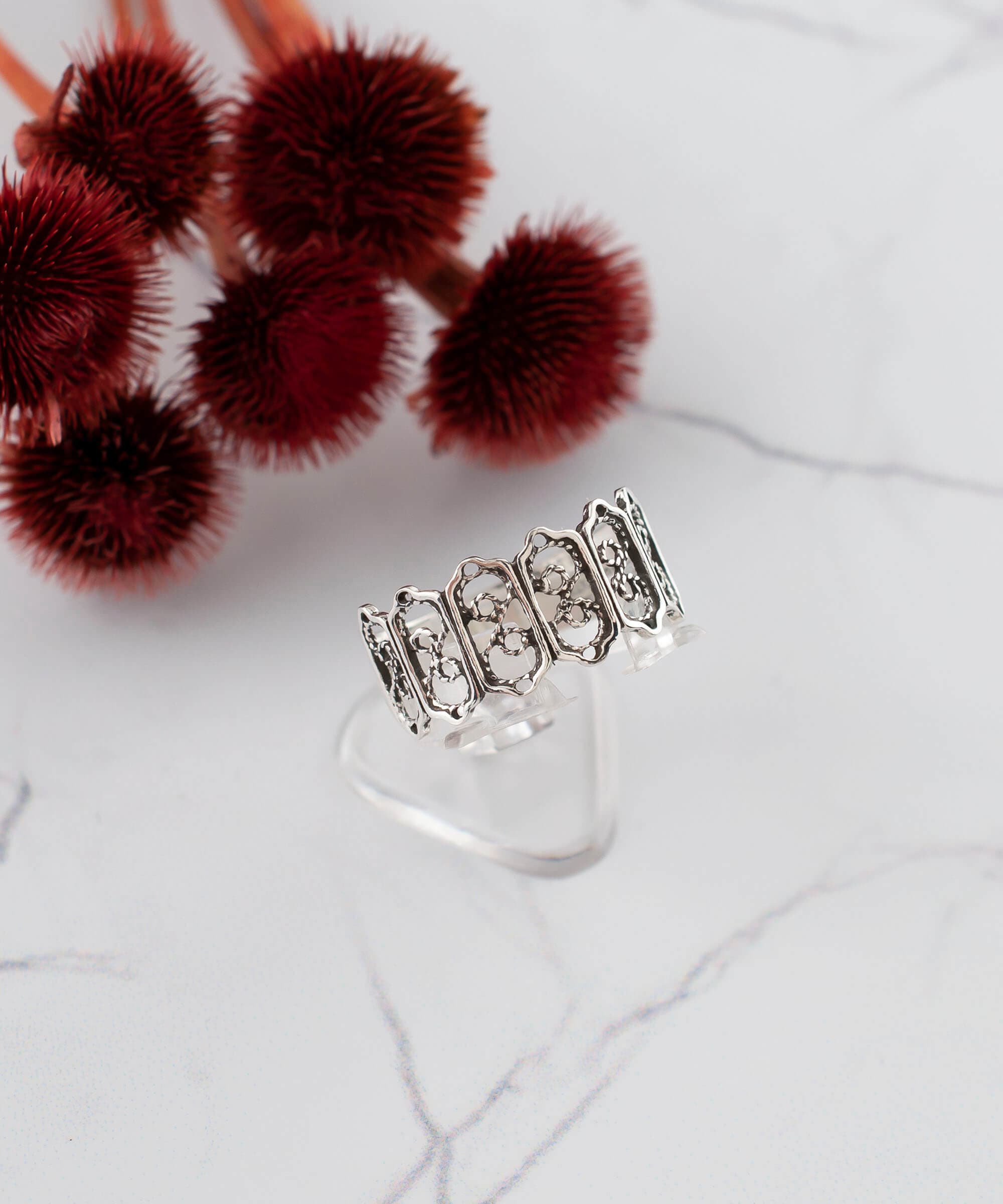 A delicate sterling silver band ring featuring intricate filigree art design, showcasing a polished and oxidized finish.