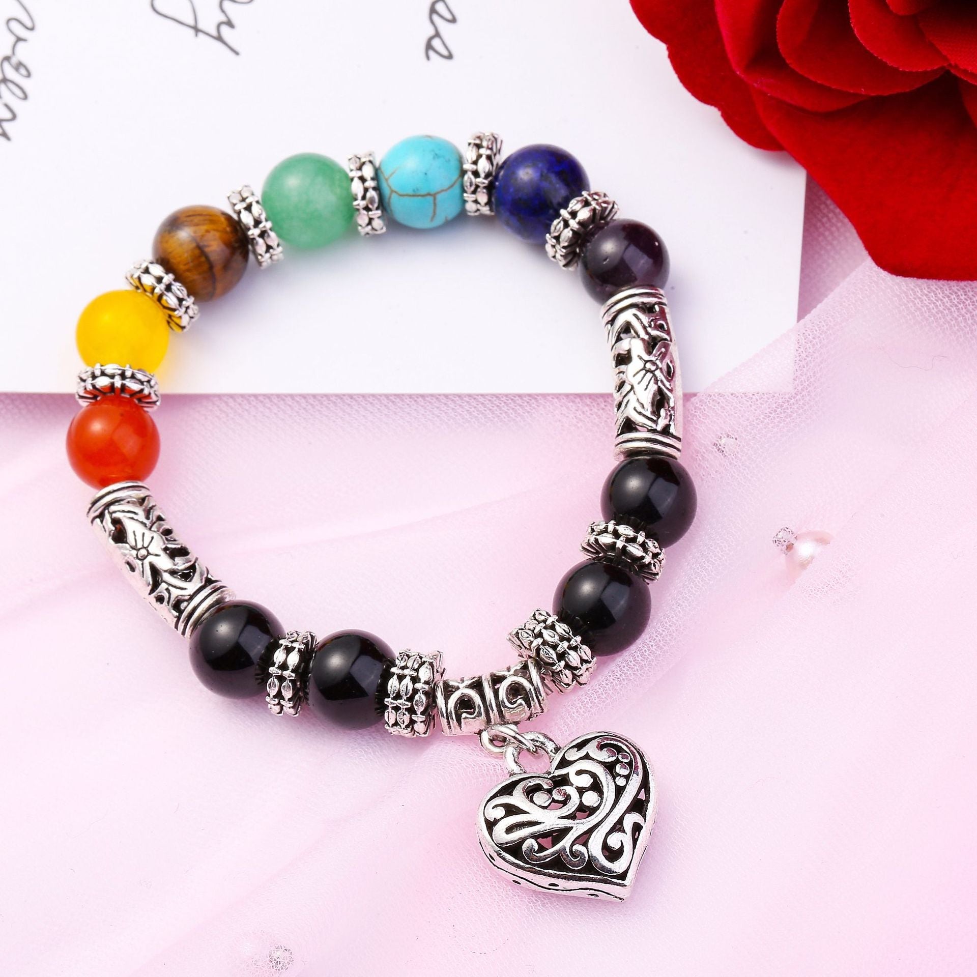 A beautiful silver plated brass bracelet featuring a filigree heart design and vibrant rainbow chakra colors, perfect for women.