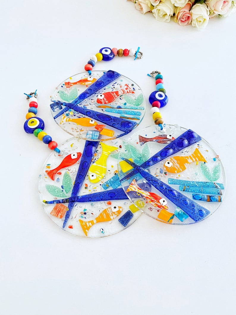 A vibrant Fish Evil Eye Wall Hanging made of fused glass, featuring a unique design with a protective evil eye motif, measuring 12cm x 12cm.